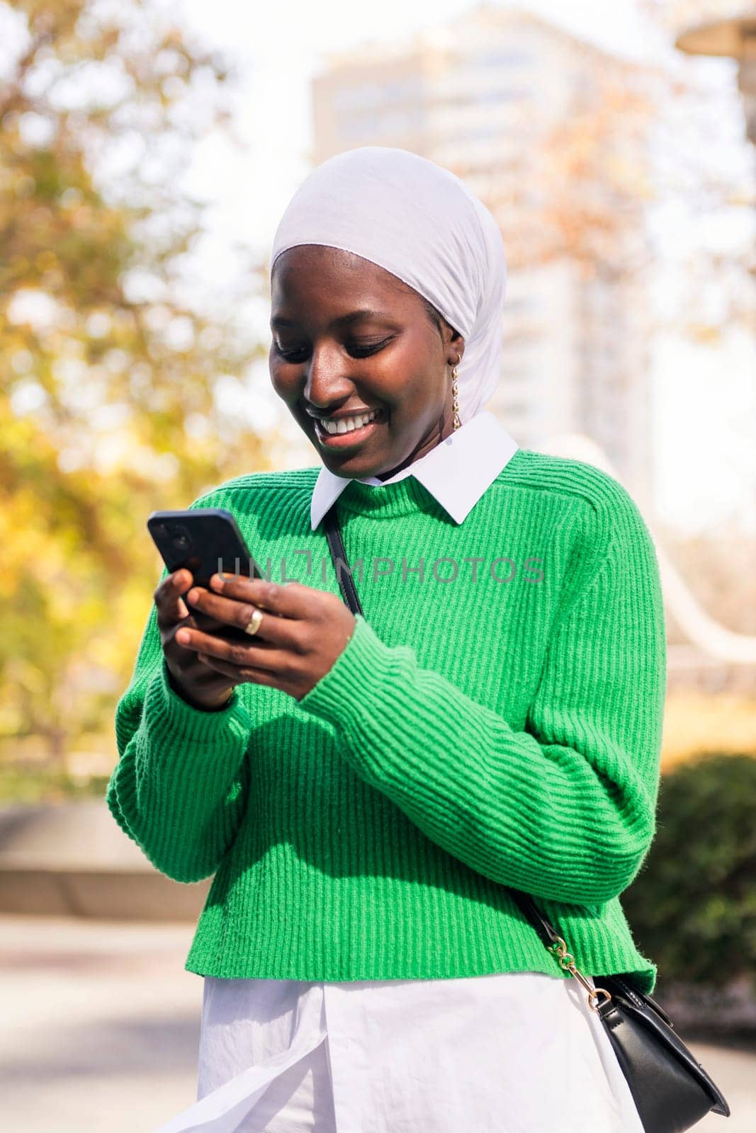 muslim black woman smiling happy using her mobile phone, concept of technology and modern lifestyle