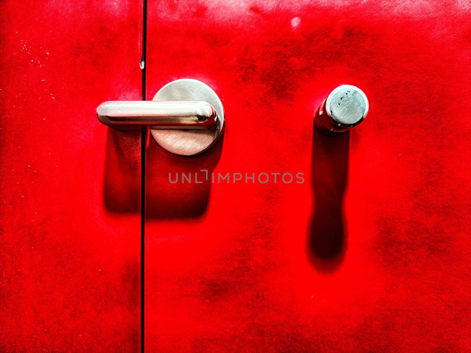 Close-up of a shiny metallic door handle and a latch set against a crimson backdrop. Close-Up of a Chrome Handle and Latch on a Vibrant Red Door by keleny