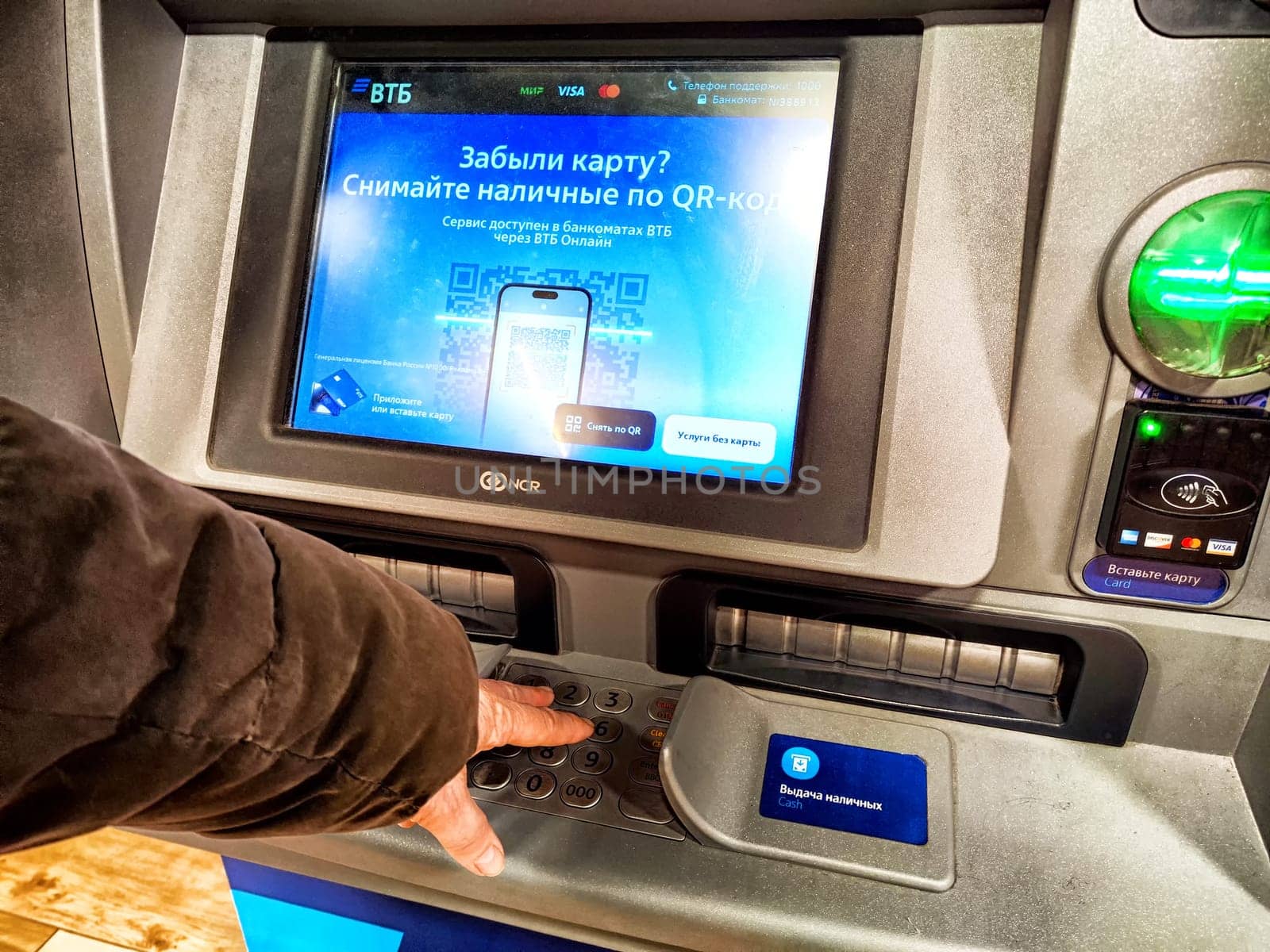 Kirov, Russia - April 28, 2024: Person Withdrawing Cash From ATM in Russia. Hand pressing button on an ATM with a Russian language screen