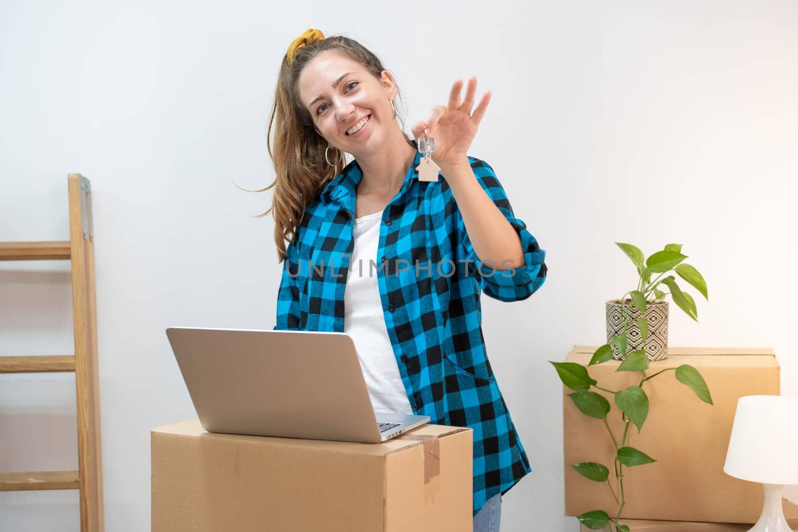 Portrait of happy young attractive woman with laptop on cardboard boxes moving in a new home. New house keys, new life. High quality photo