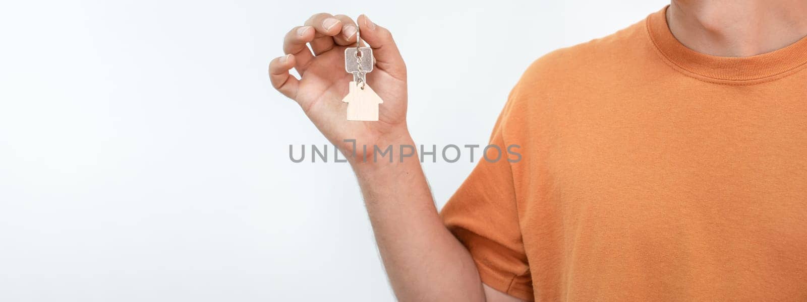 Banner of young man with the new home keys. Keychain in the shape of a wooden house on white background. High quality photo