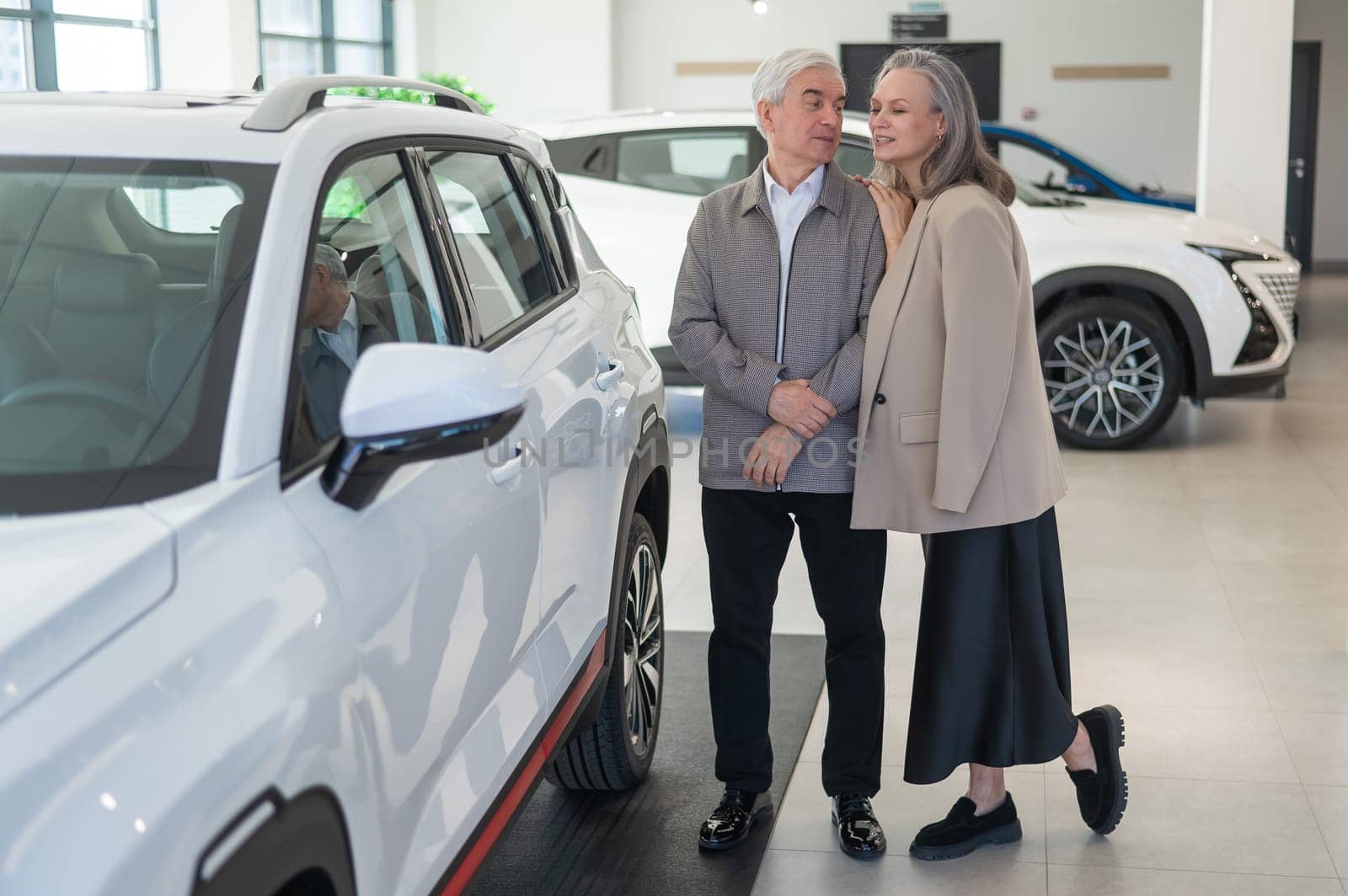 An elderly Caucasian couple chooses a new car at a car dealership