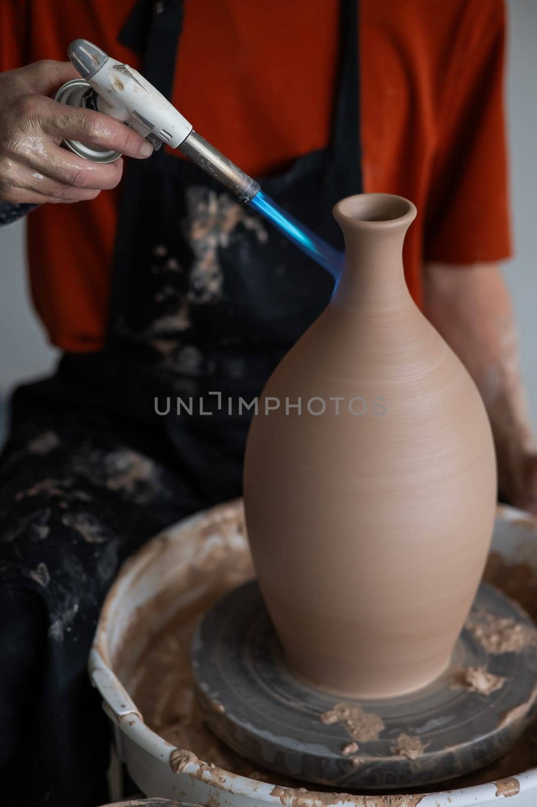 Close-up of a potter's hands firing a jug with a gas burner on a potter's wheel. Vertical photo. by mrwed54