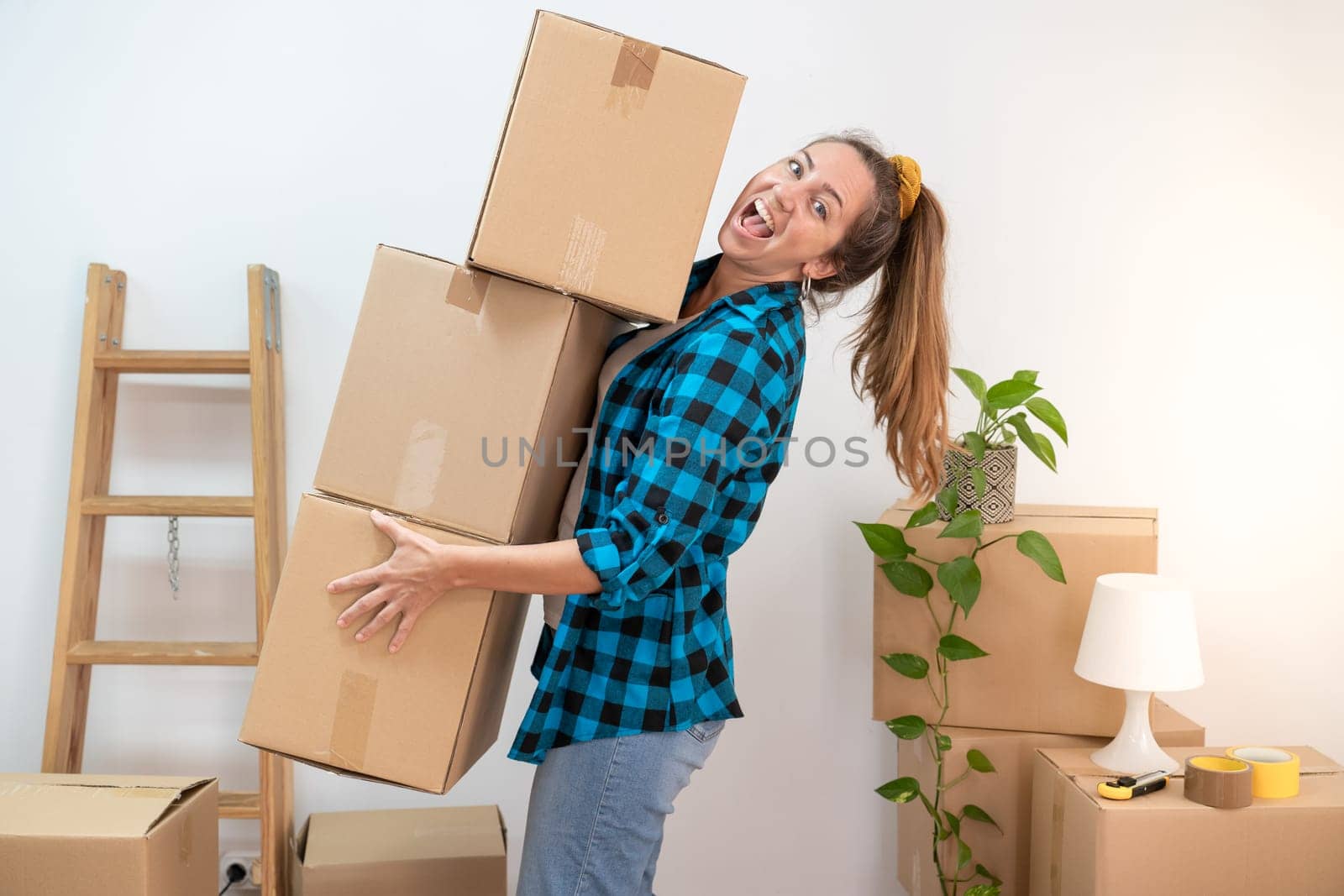 Young woman with big smile carrying heavy cardboard boxes in house. Moving to new home concept. High quality photo