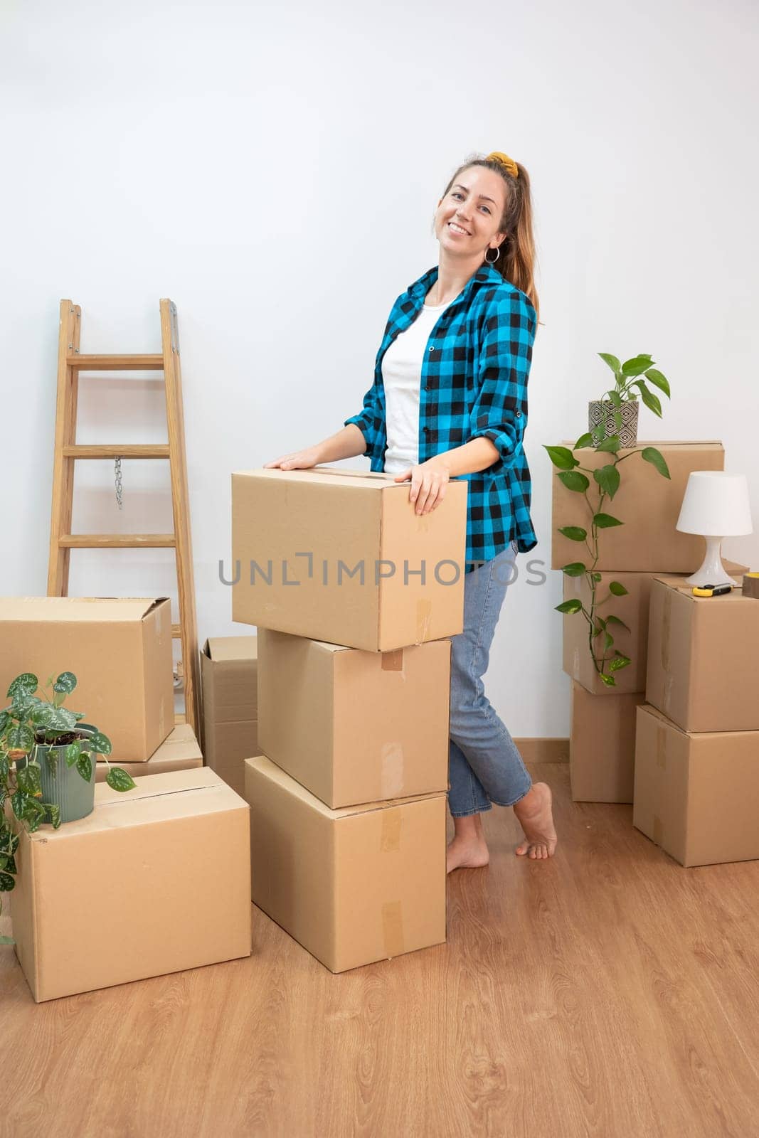 Beautiful young woman holding cardboard box at new apartment, smiling very happy moving to a new house. High quality photo