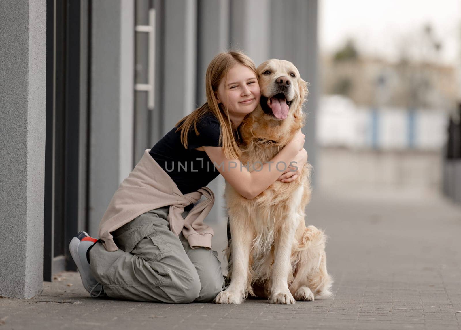 Girl Hugs Golden Retriever Sitting On Street In Summer