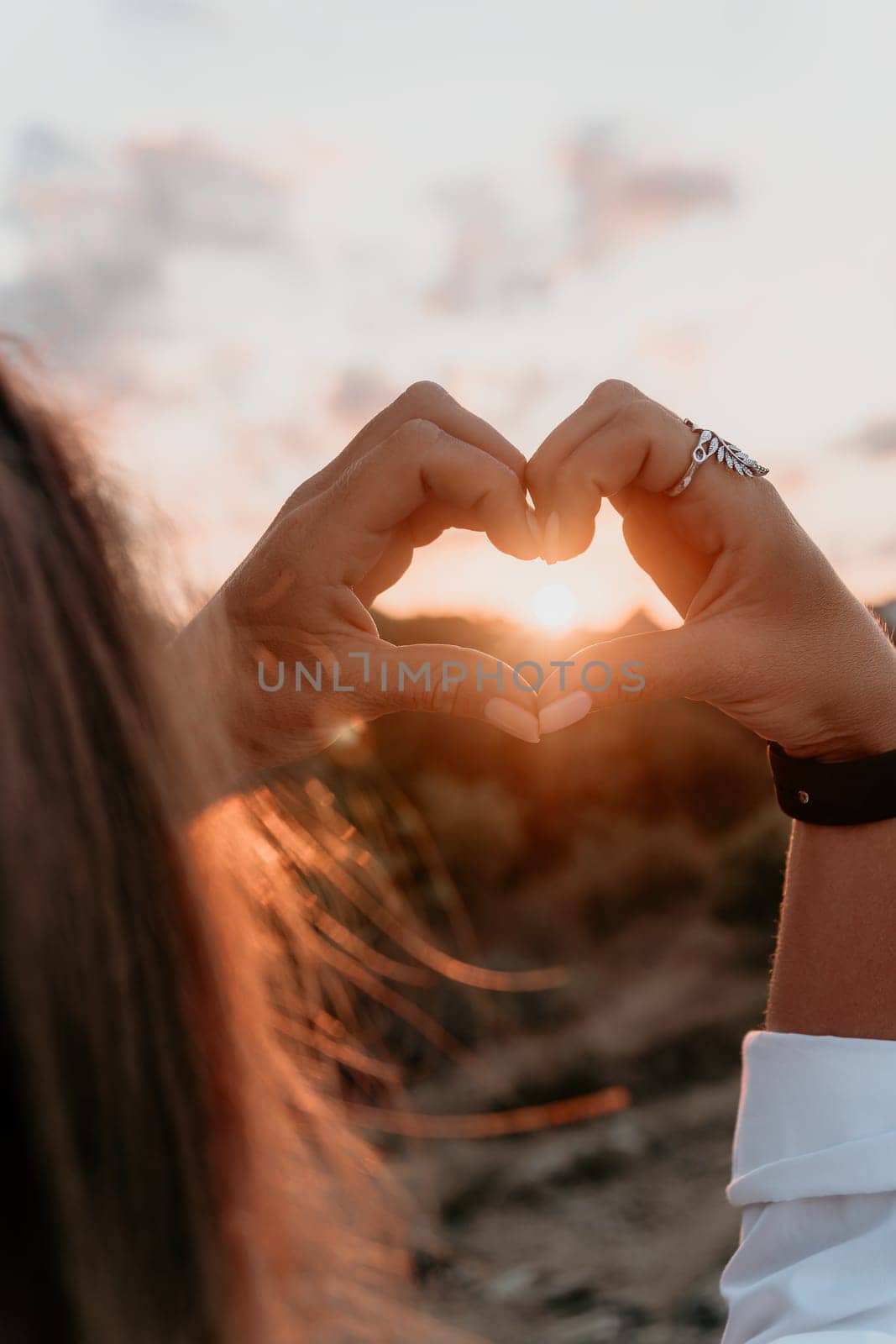 A woman's hand is holding a heart shape, with the sun shining on it. Concept of love and warmth, as the sun symbolizes happiness and positivity. The heart shape represents the bond between two people