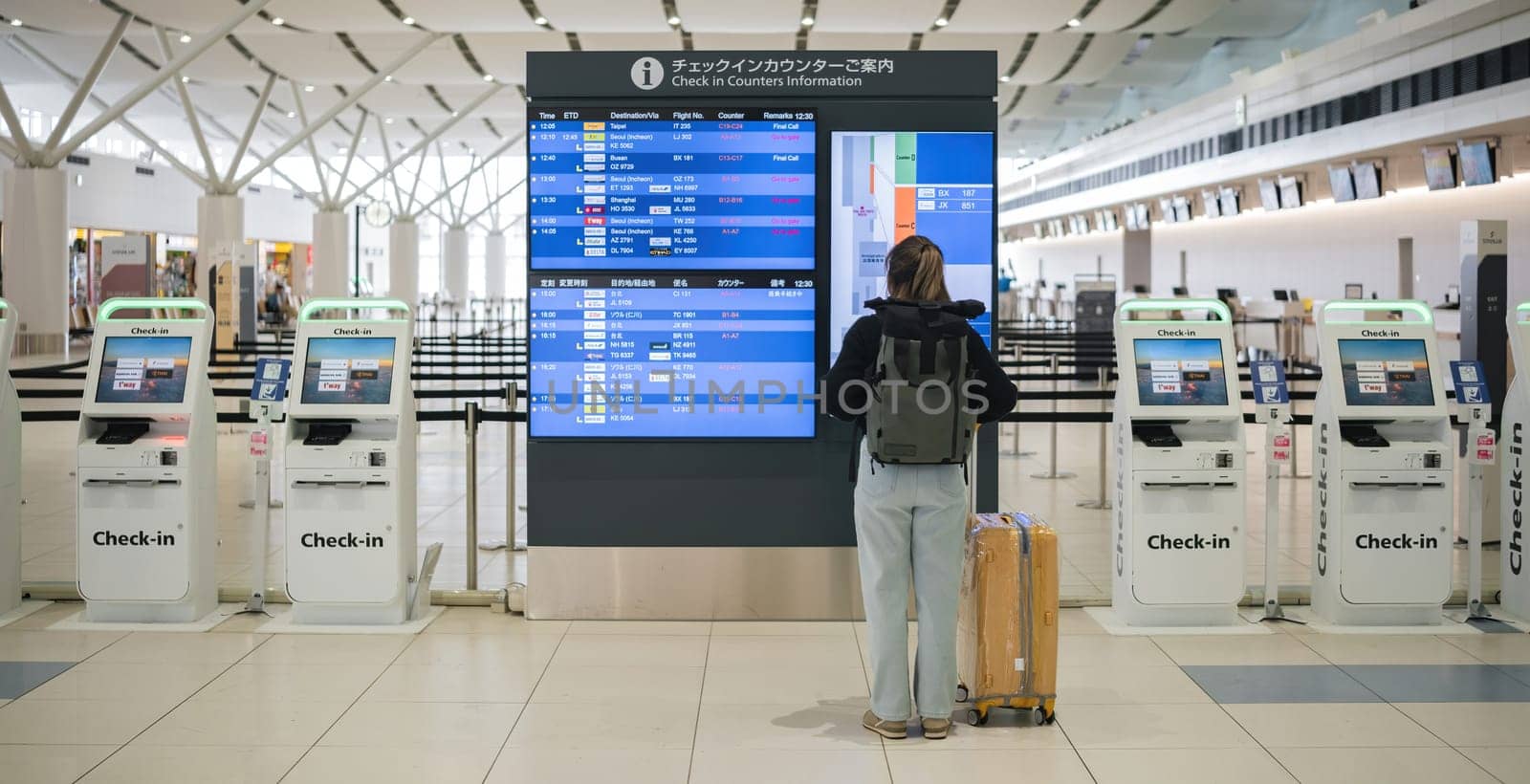 Young Asian woman in international airport looking at flight information board, checking her flight.