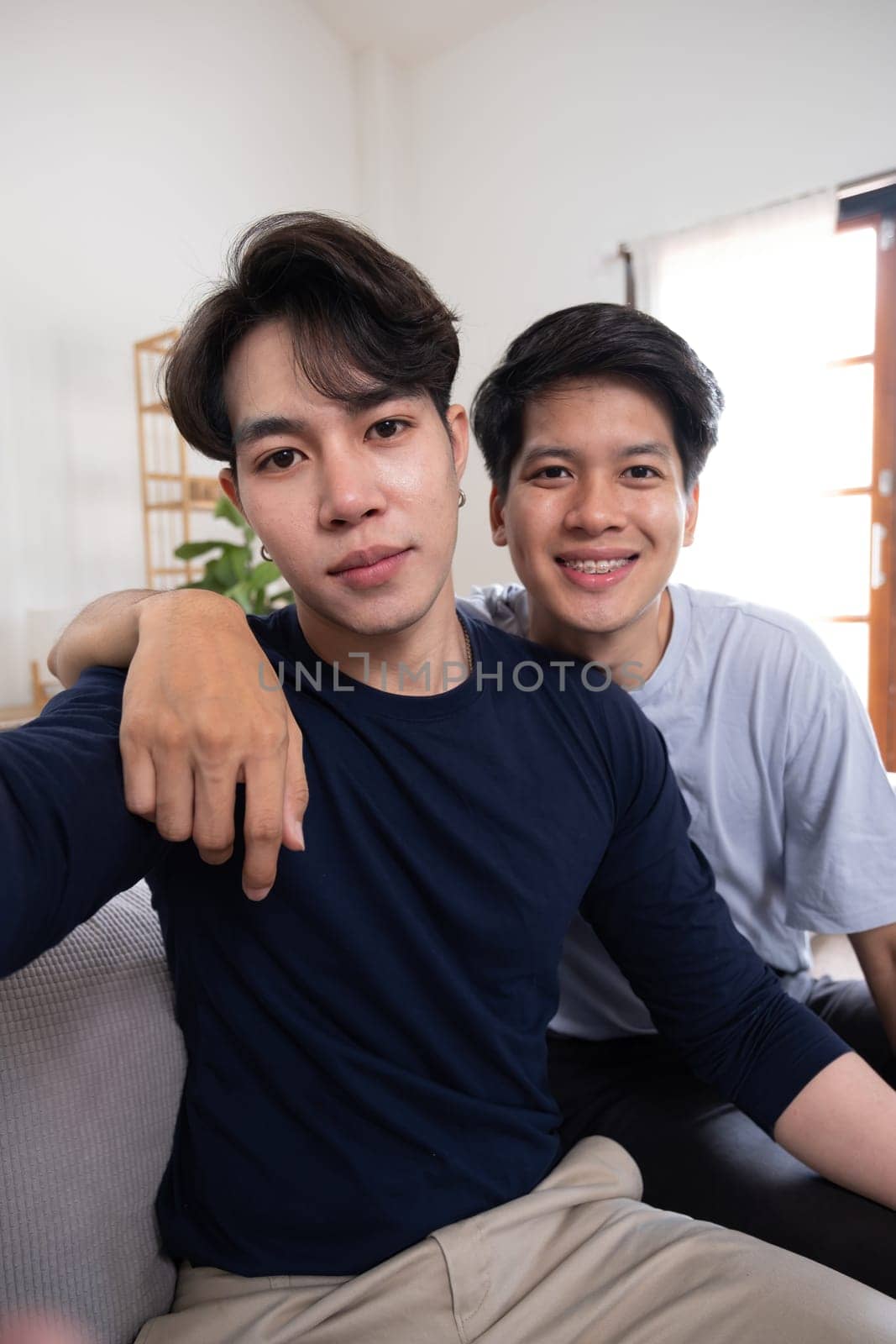 A male-male couple spends their free time happily doing holiday activities together, embracing each other and taking selfies together in the living room. by wichayada