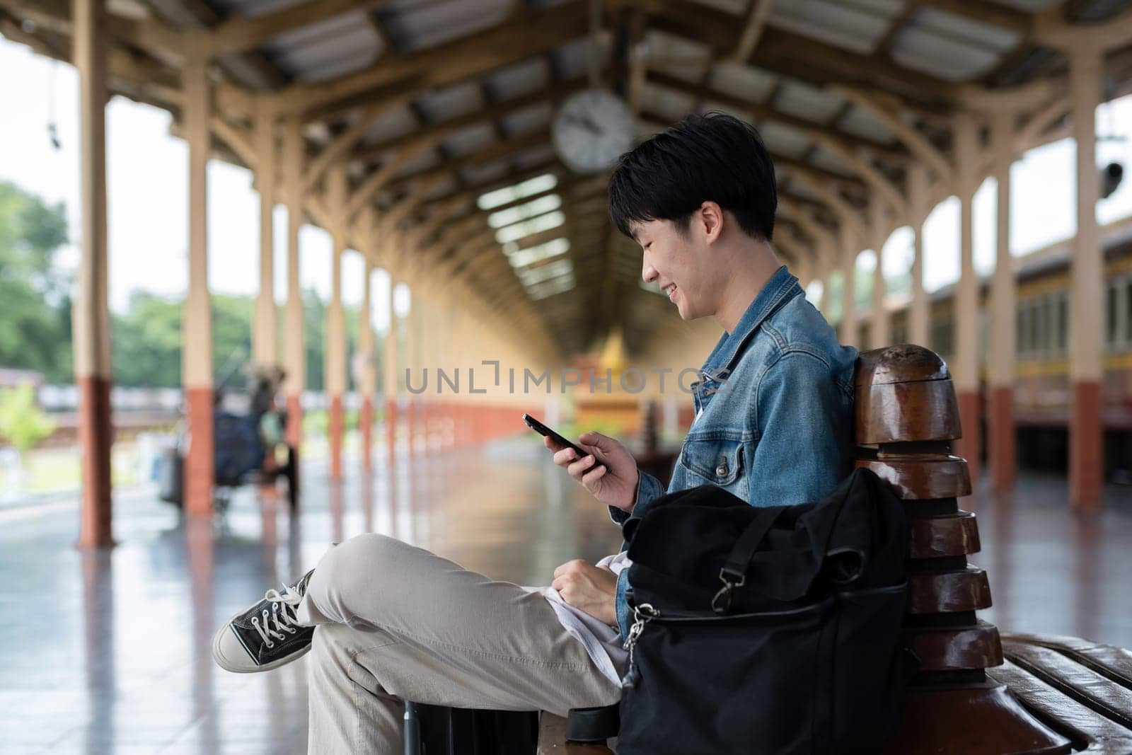 Young man with backpack checking social media on phone waiting for train at train station to travel.
