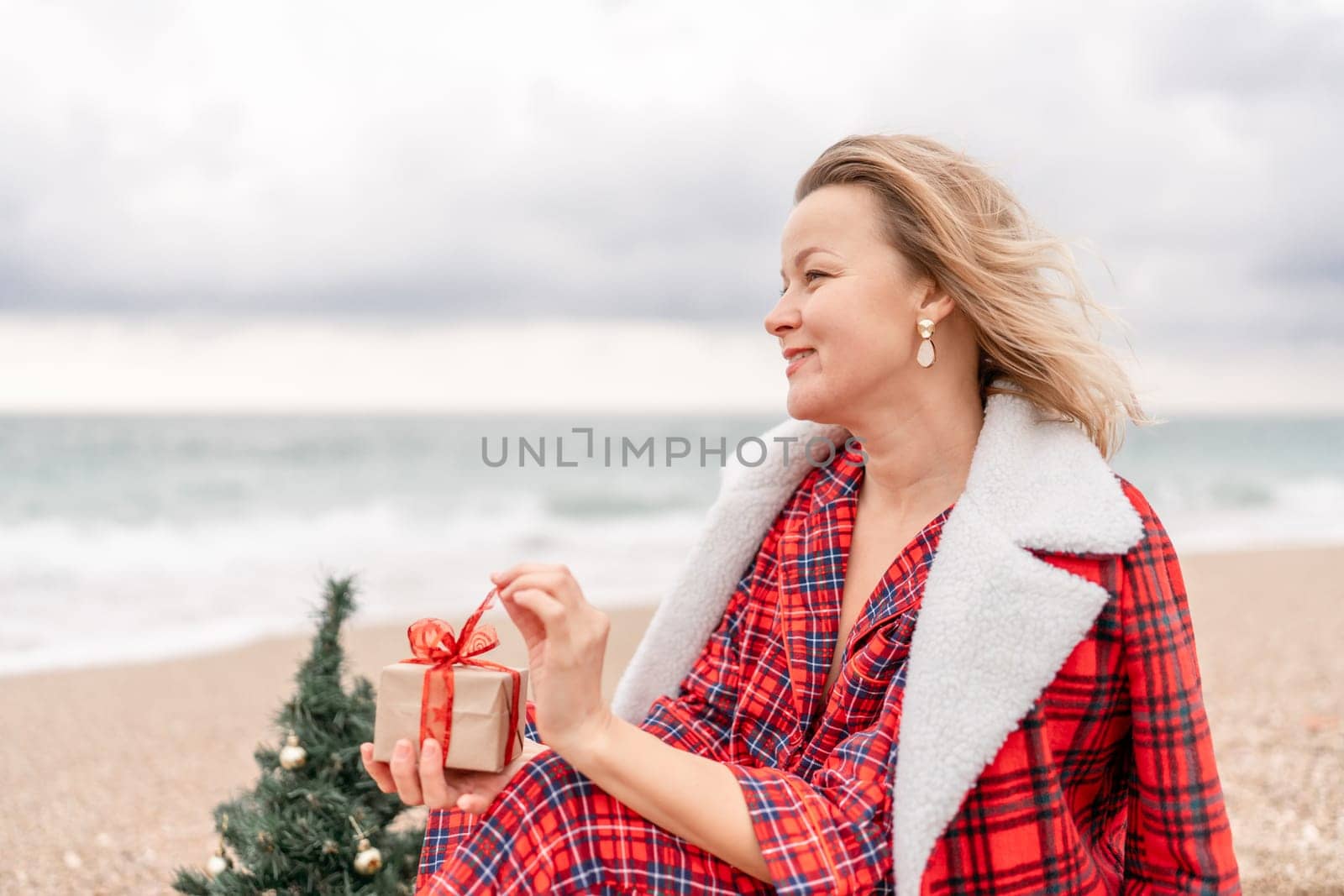 Lady in plaid shirt holding a gift in his hands enjoys beach with Christmas tree. Coastal area. Christmas, New Year holidays concep by Matiunina