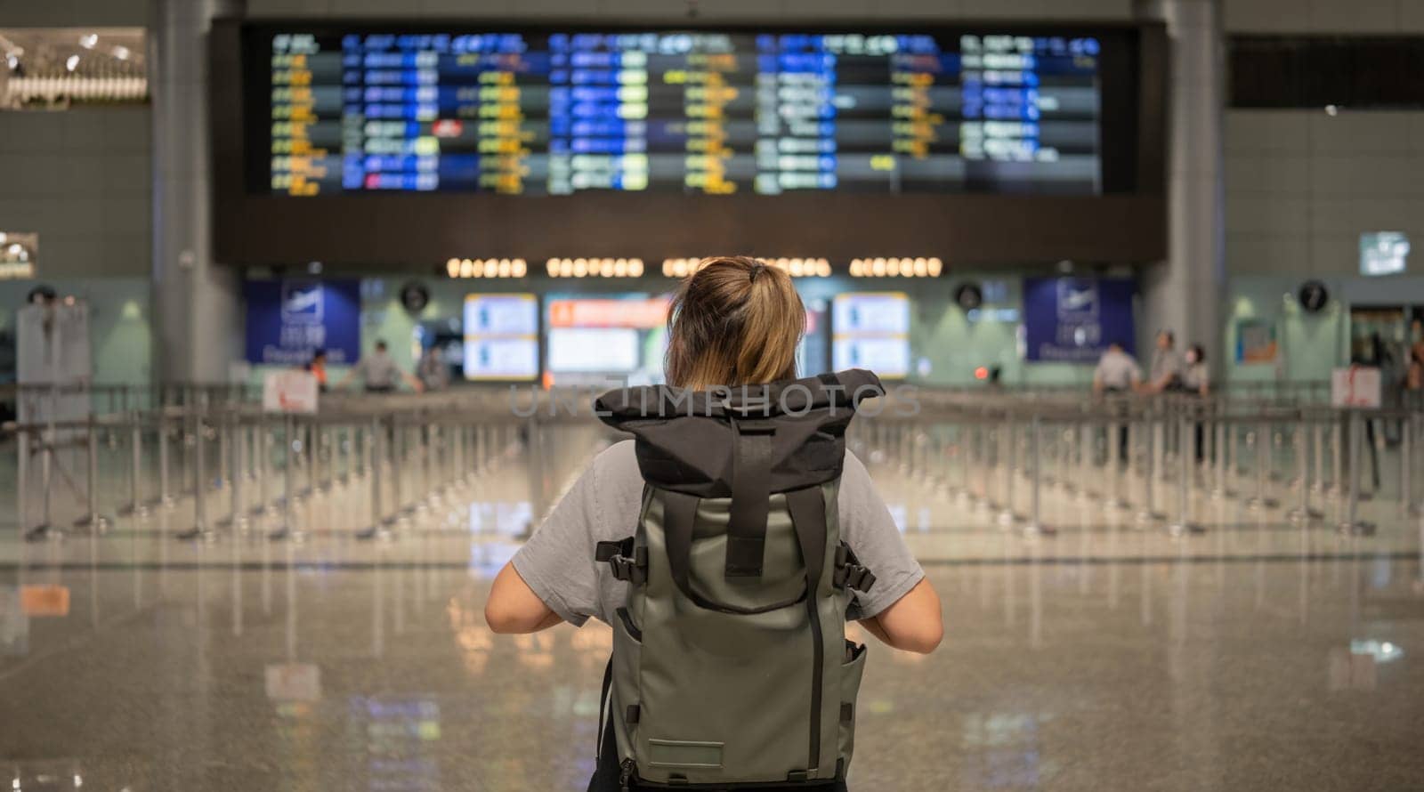 Young Asian woman in international airport looking at flight information board, checking her flight by wichayada