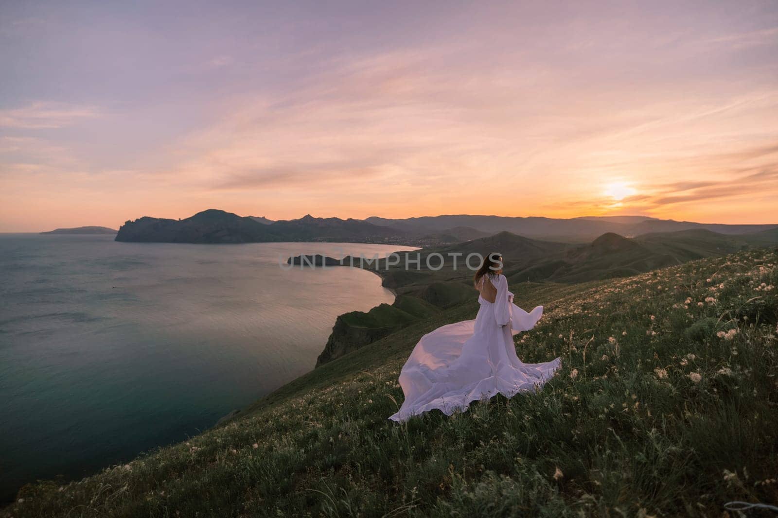 A woman in a white dress is walking on a grassy hill overlooking a body of water by Matiunina