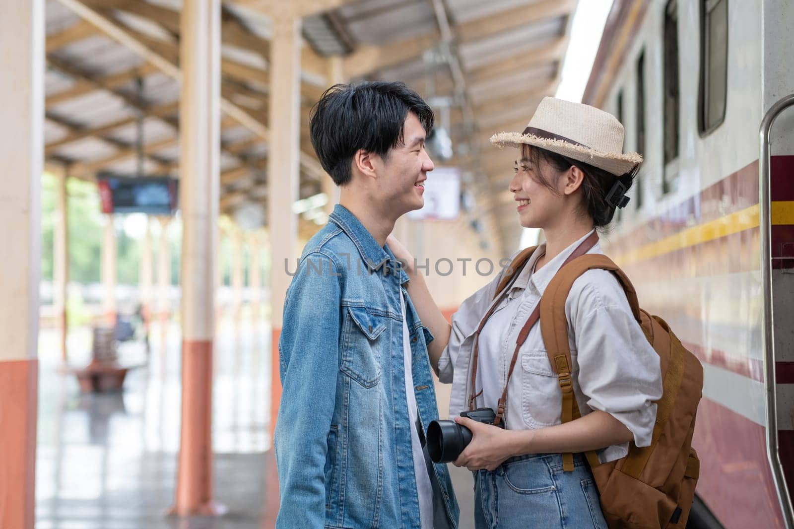 Happy Asian couple holding suitcases and camera preparing to wait for train at train station for vacation trip together. by wichayada