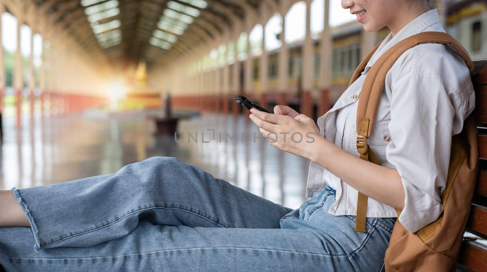 Young woman with backpack checking social media on phone waiting for train at train station to travel.