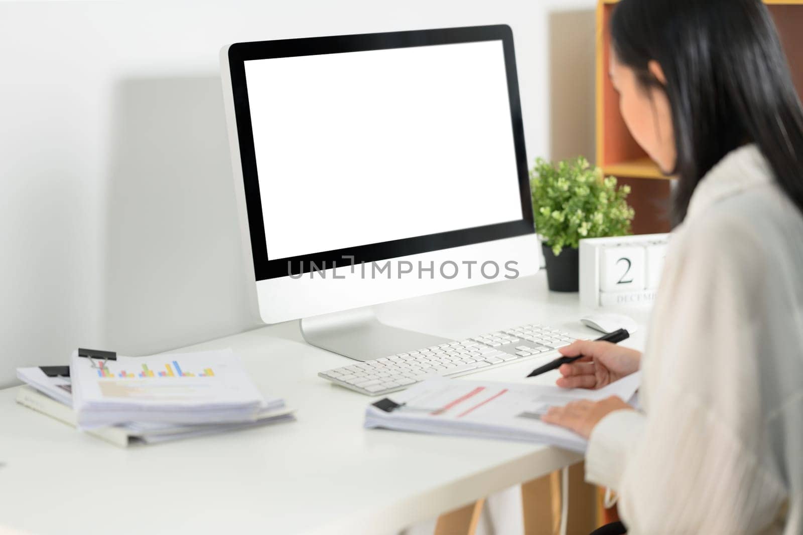 Side view of female accountant sitting at her workplace in front of blank computer monitor.