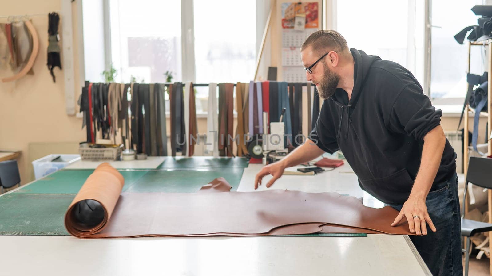 Leatherworker unrolls rolls of leather in workshop