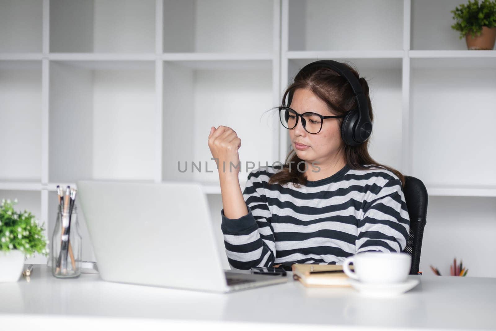A young woman who is bored from studying online at home wears headphones while studying in an online class..
