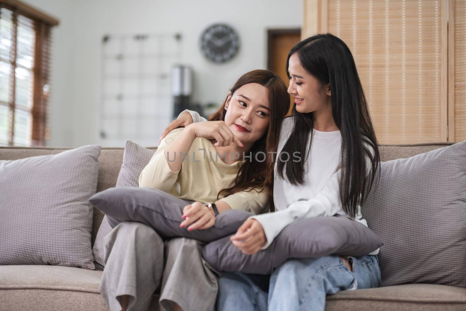 Young LGBT woman, lesbian couple, sitting on the sofa, hugging and smiling happily together in the living room at home. by wichayada