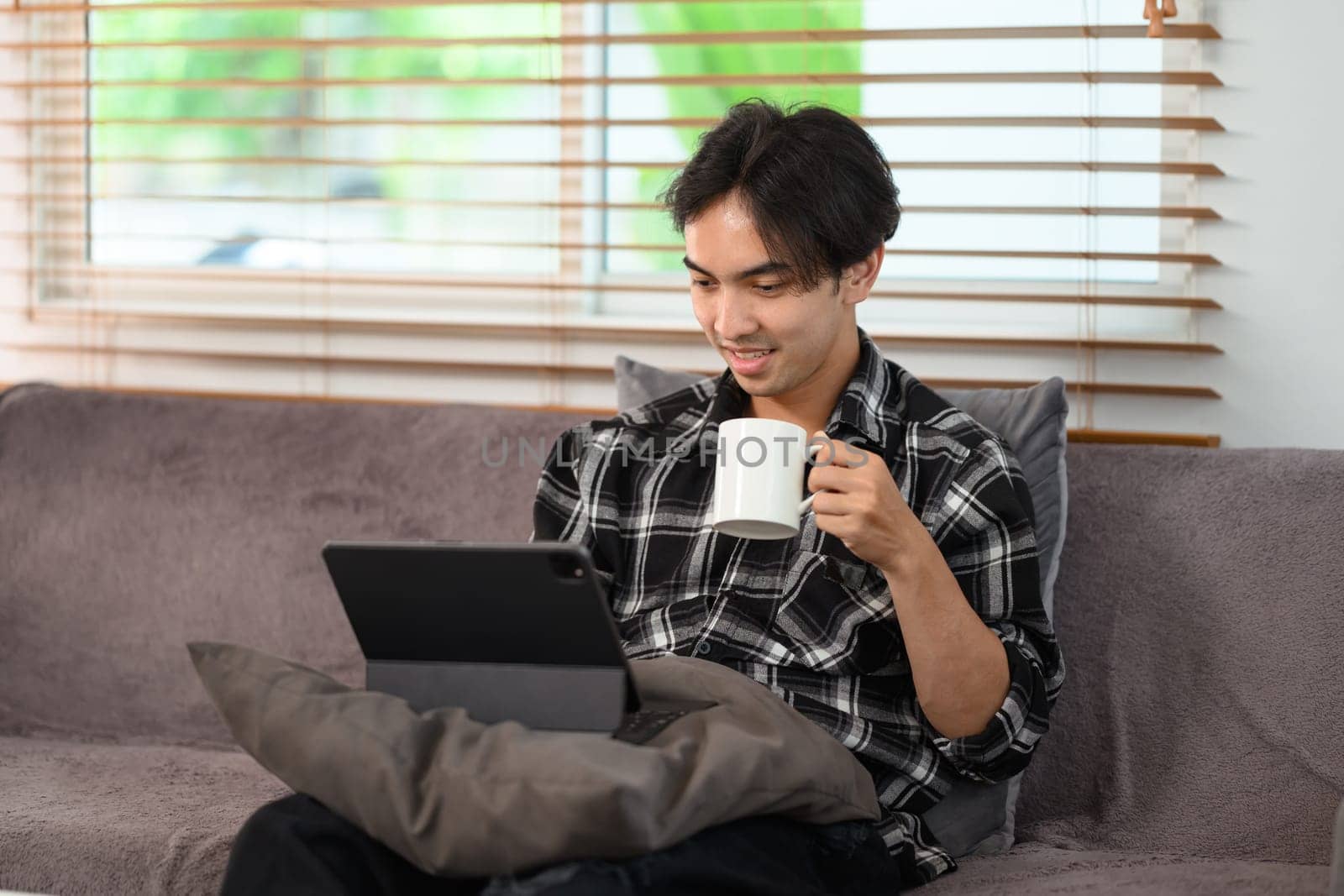 Happy young man drinking coffee and surfing internet on digital tablet at home by prathanchorruangsak