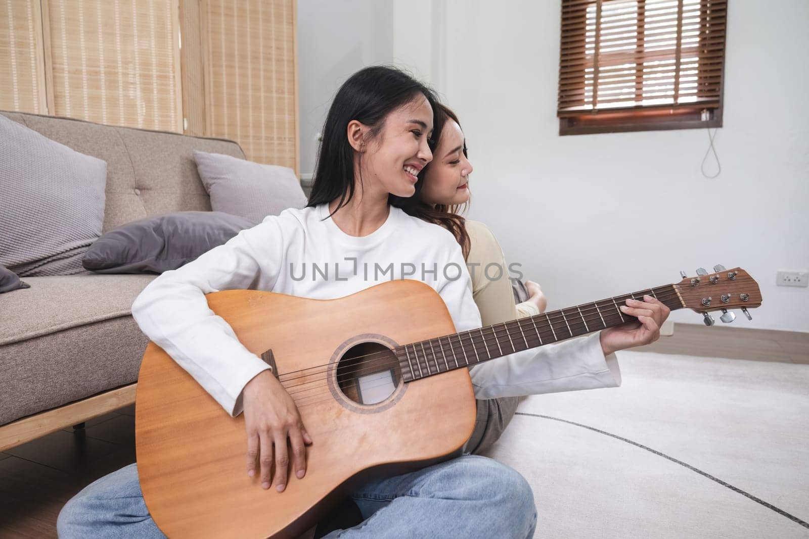 Young LGBT woman, lesbian couple, playing guitar together in the living room..