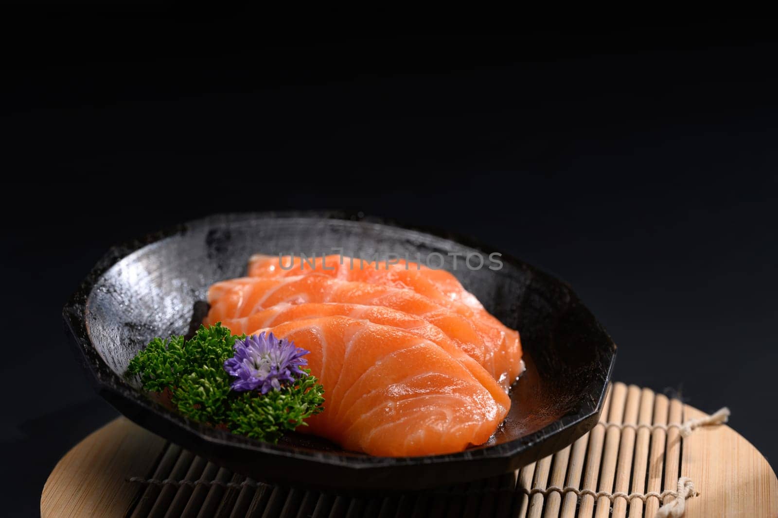 Close up sliced salmon sashimi serve on black plate with parsley leaf. Japanese food style by prathanchorruangsak