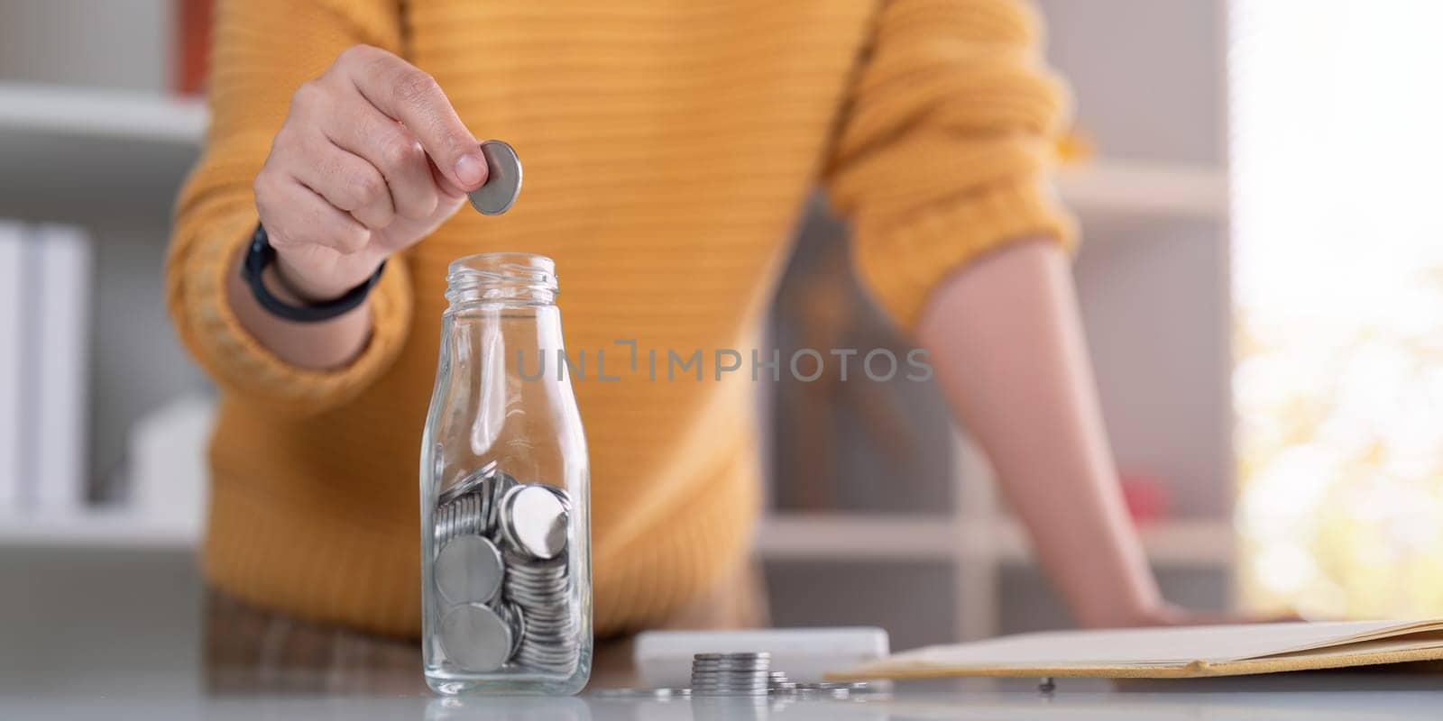 Woman saving money with hand putting coins in jug glass concept finance and accounting finance and saving money for future concept by nateemee