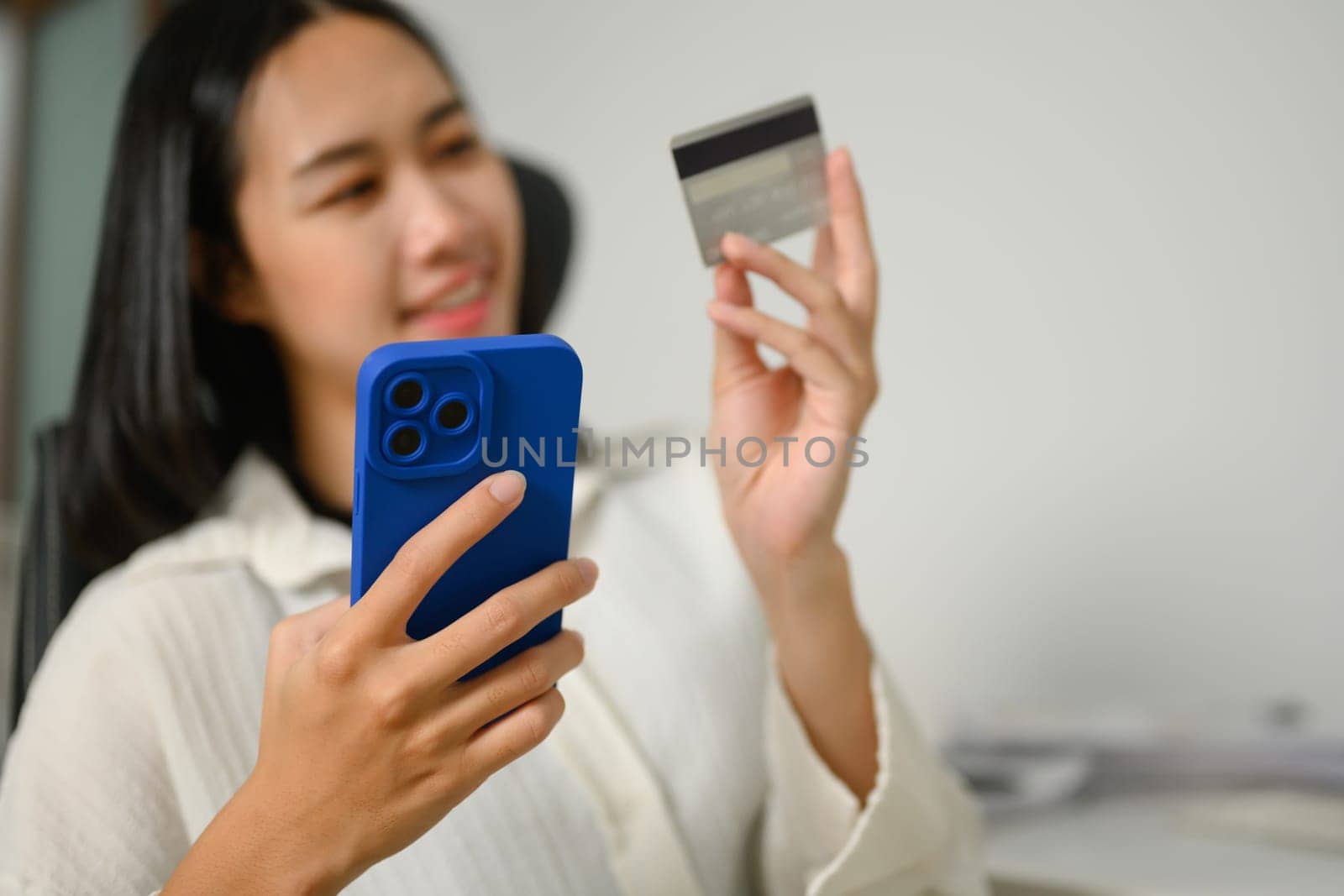 Happy young woman with credit card making internet order purchase on mobile phone by prathanchorruangsak