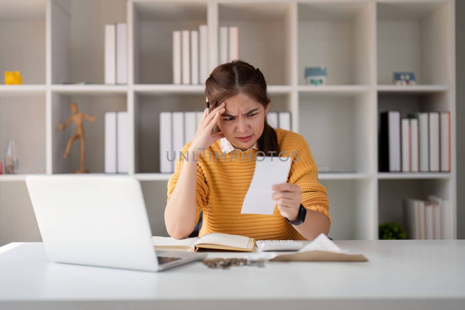 Stress asian young woman calculate tax, income and expenses, hand holding bill of payment or payday on table at home office. Financial, finance people concept.