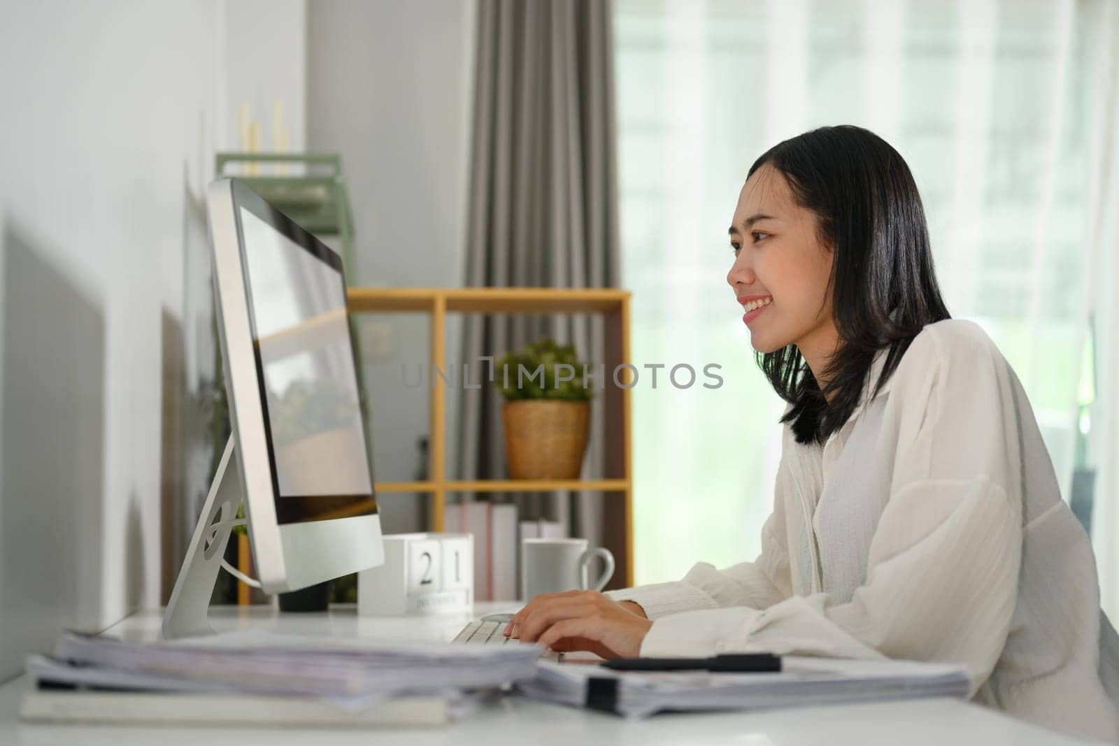 Young businesswoman typing on computer keyboard answering business email in the morning by prathanchorruangsak