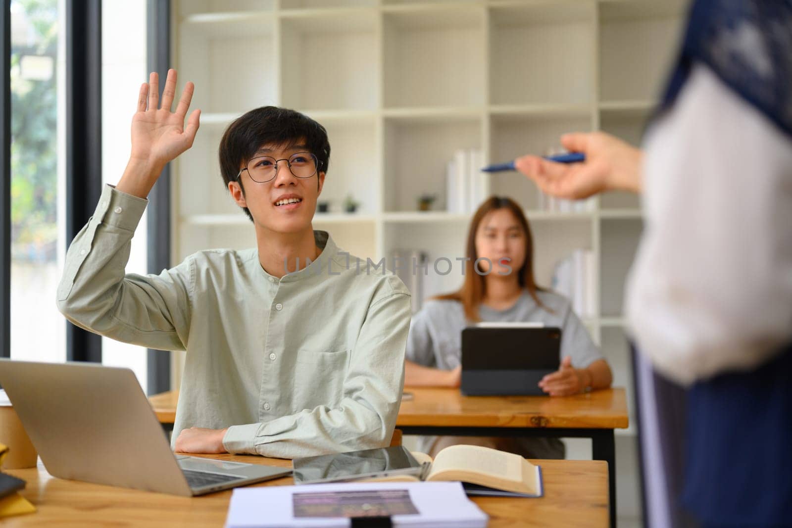 College student man raising his hand to answer question or ask something during class by prathanchorruangsak