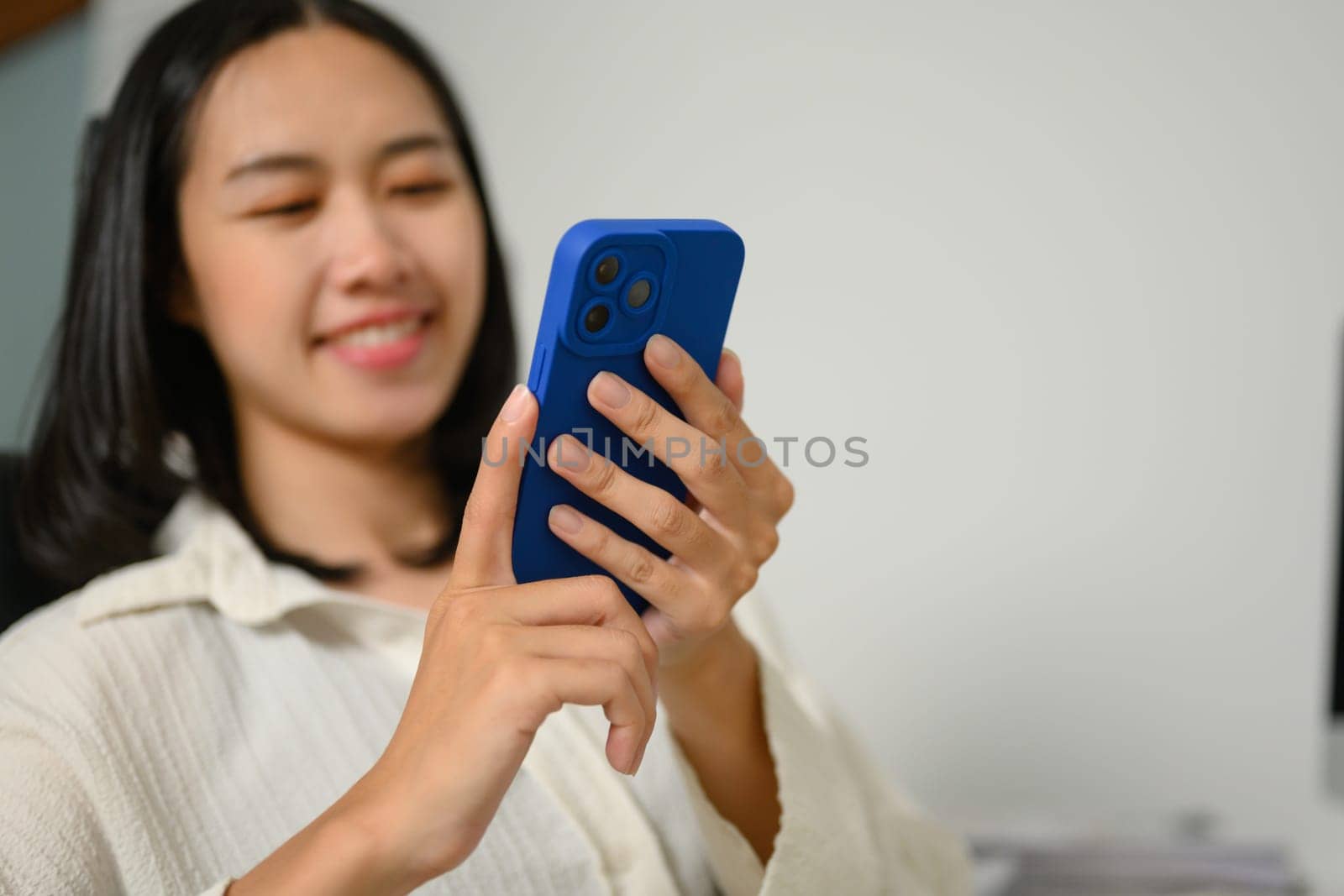 Smiling young female worker sitting at desk and using mobile phone.