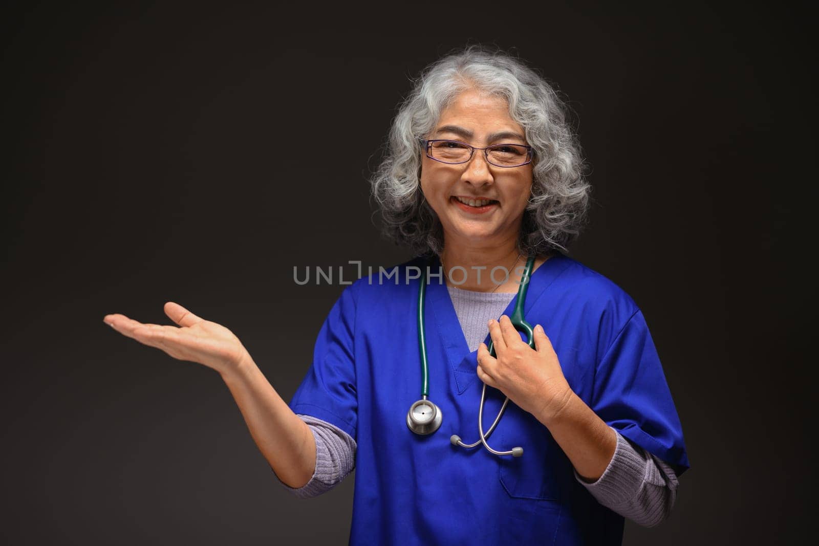 Portrait of senior doctor coat presenting and pointing with palm of hand on black background.