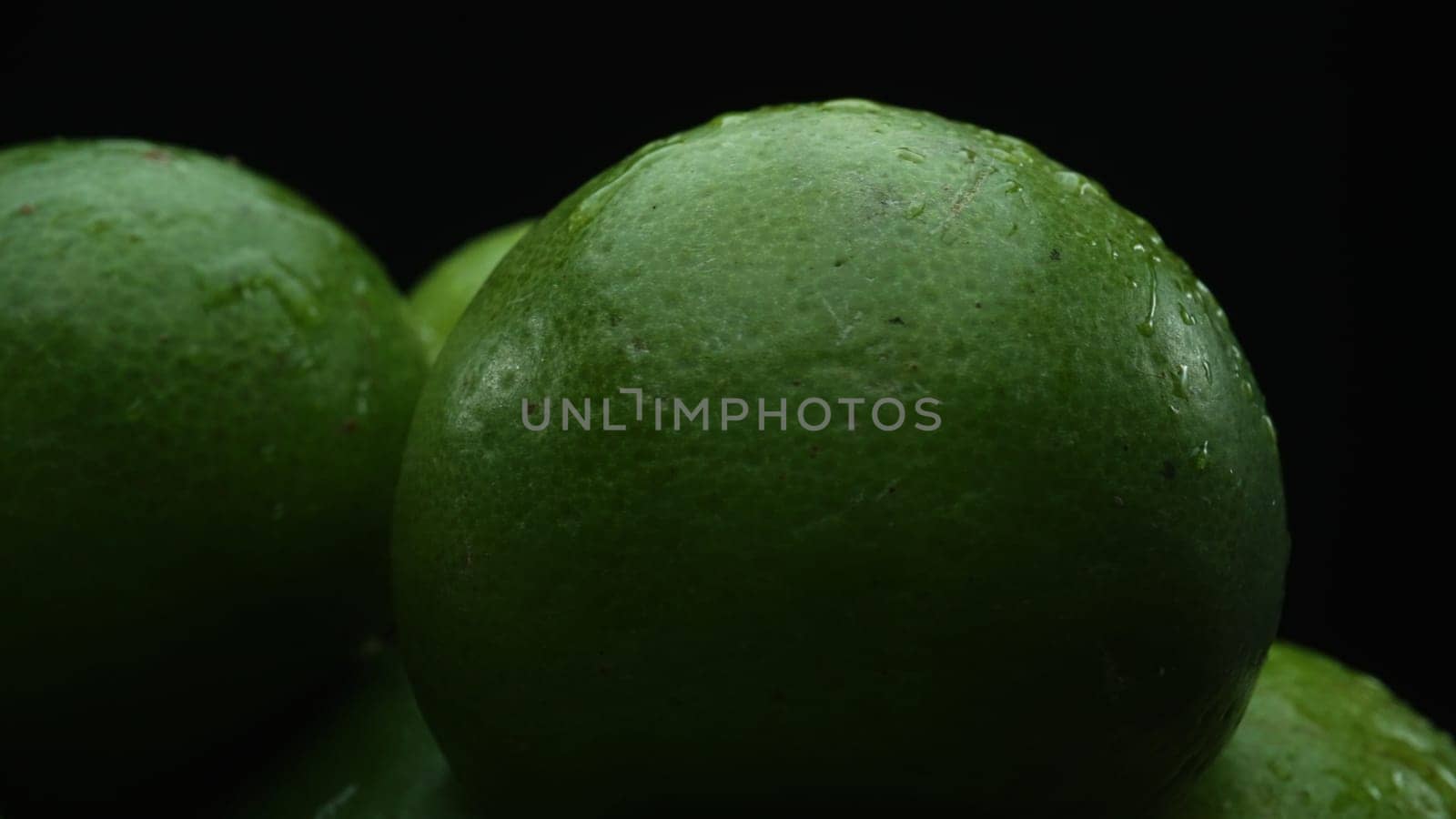 Slices of lime are meticulously arranged in a pile, set against a black background. Each lime slice is captured in stunning detail, its vibrant green hue and enticing texture. Close up. Comestible.