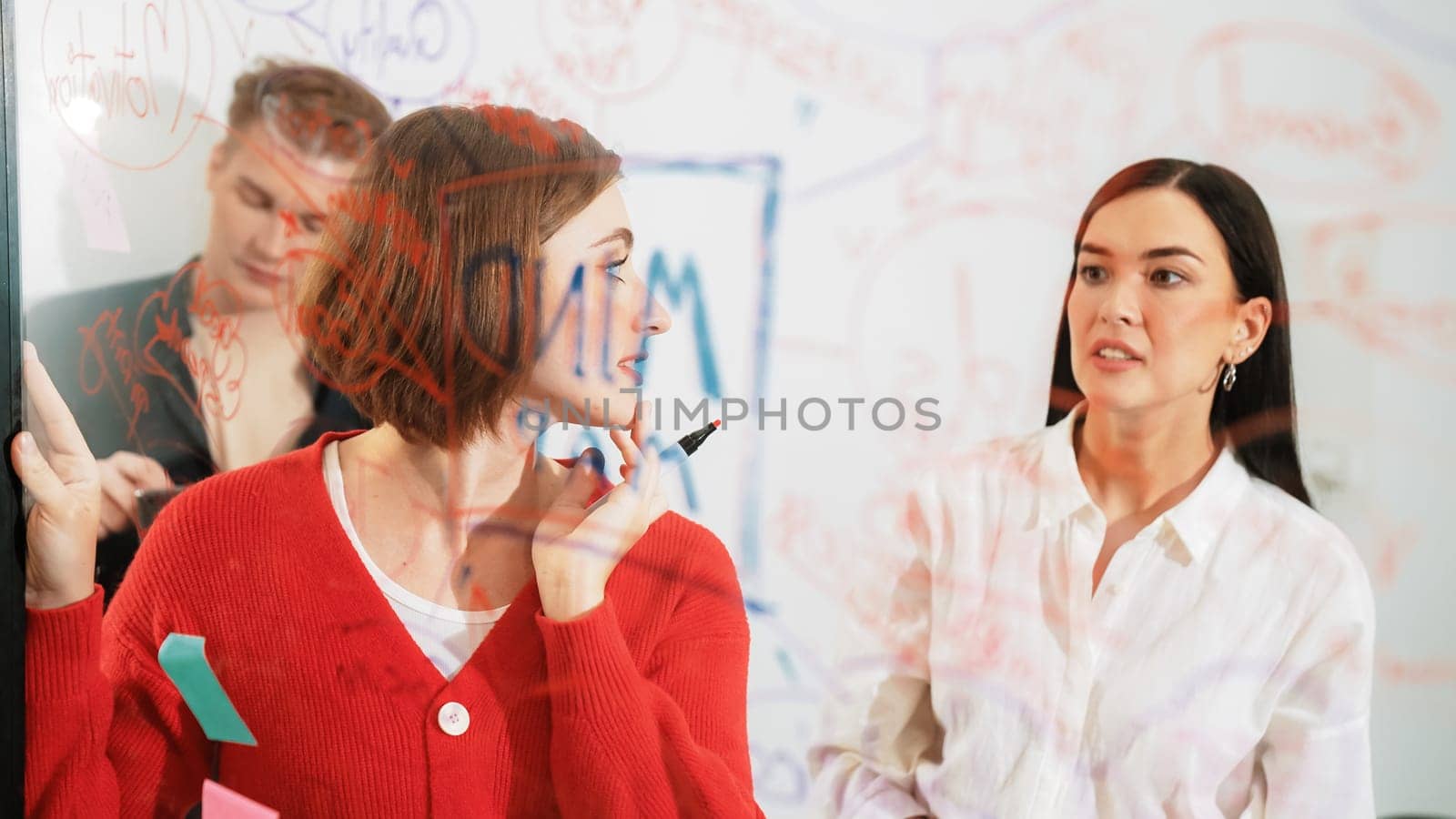 Professional business team brainstorming and working together about marketing project. Female caucasian leader writing idea on stick note while coworker present her idea confidently. Immaculate.