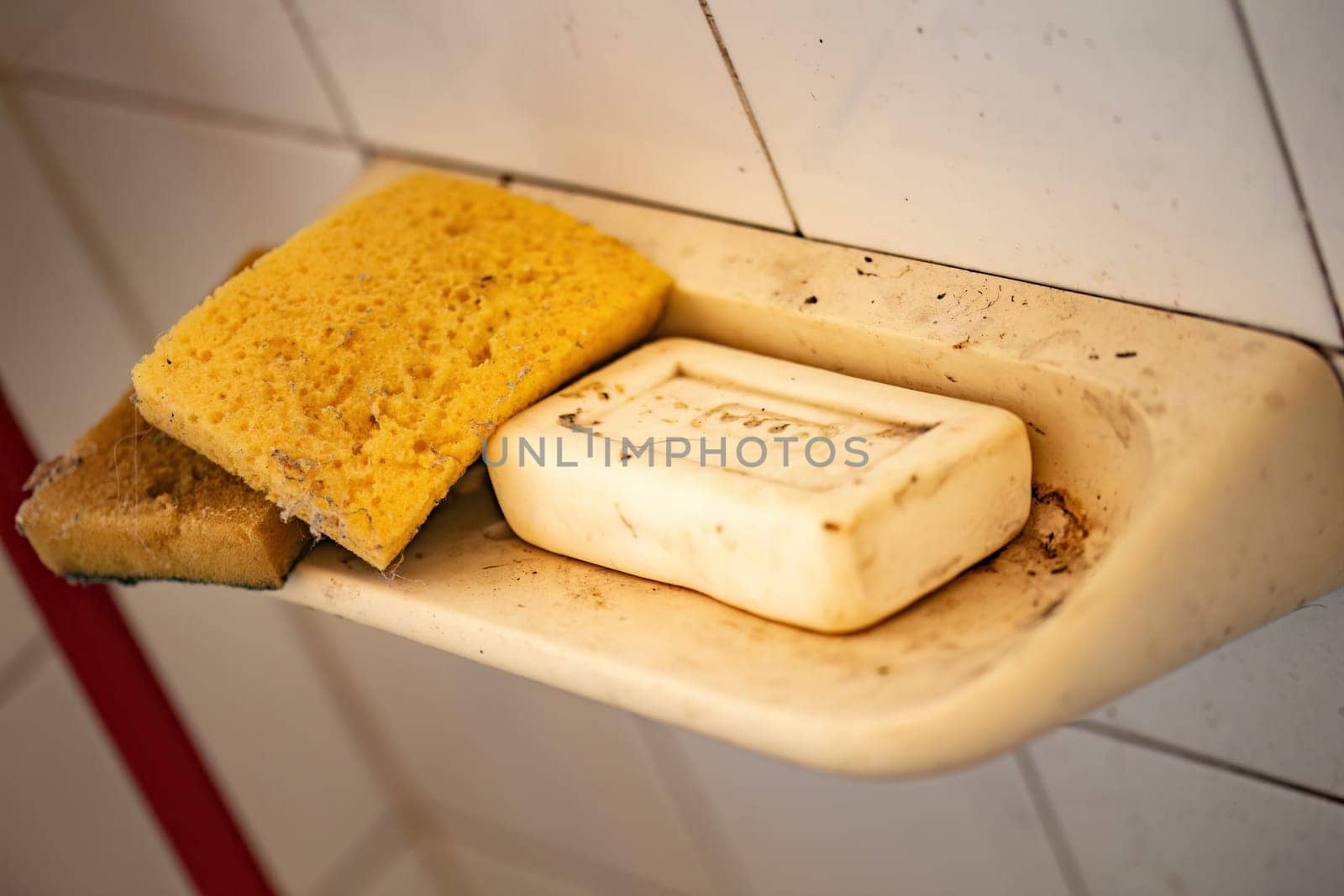 A worn and dirty soap dish holding a bar of soap and a sponge in a rustic bathroom.
