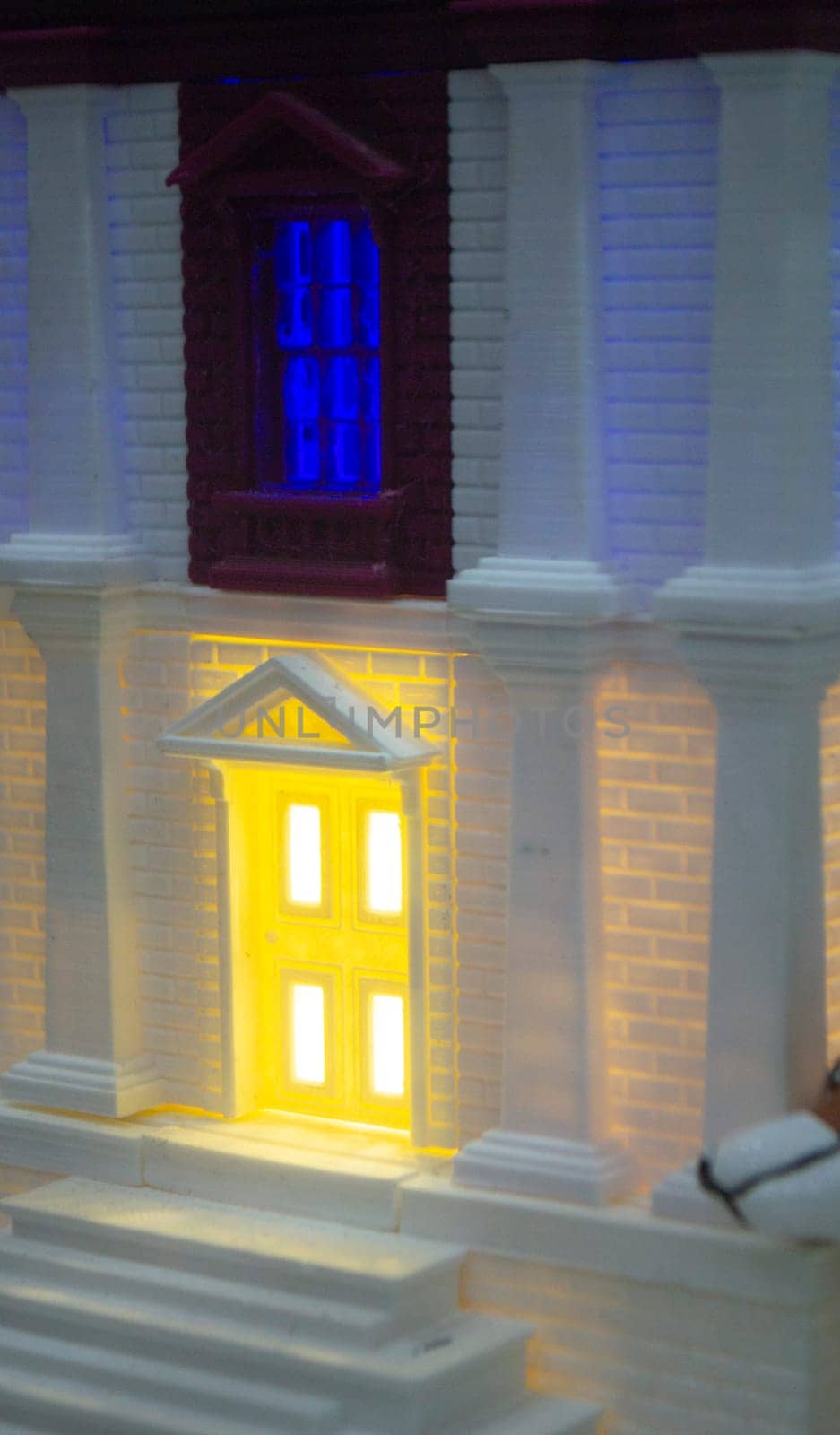 Prototype printed on 3D printer brick building with columns and glowing windows. Model of building with white and brown color, windows with light shining, created by 3D printer from molten plastic