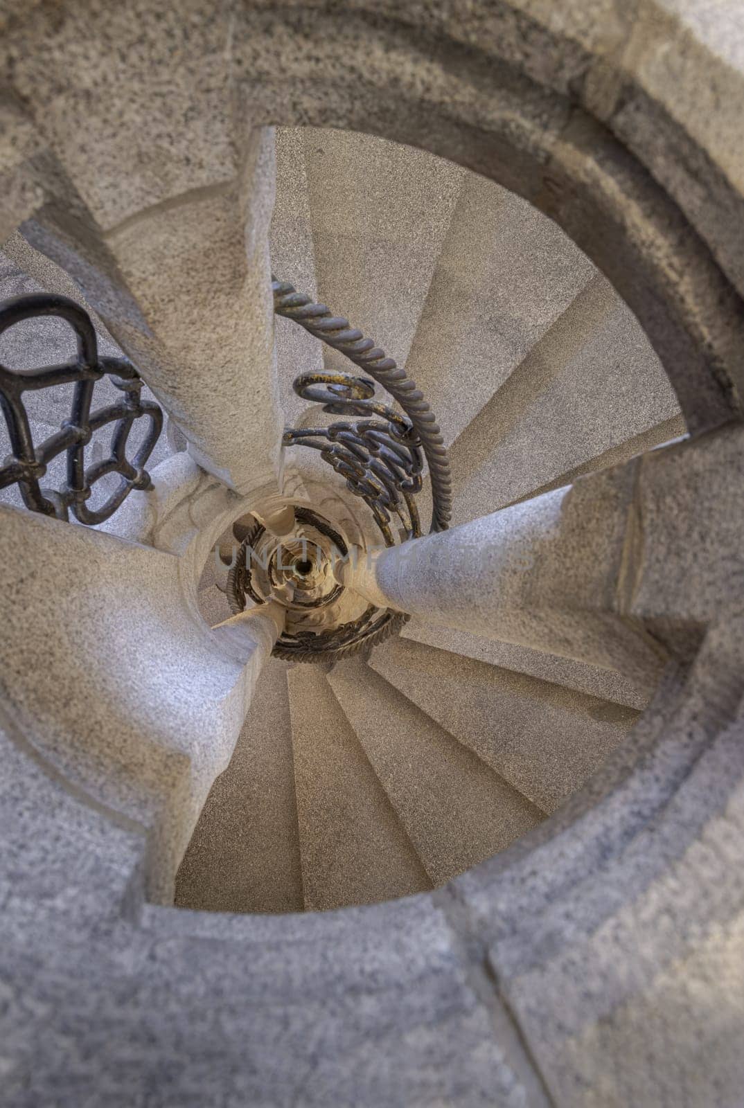 Upside view of The old stone spiral staircase with Wrought iron railing inside columnar structures.  by tosirikul