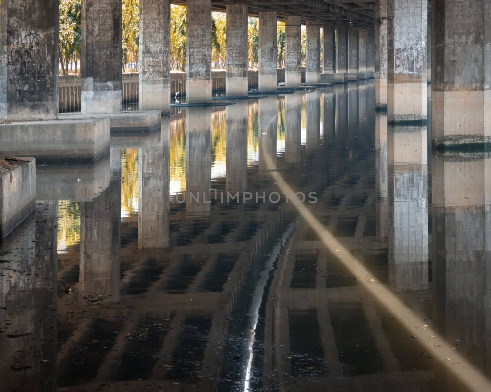Bangkok, Thailand - Apr 20, 2024 - Perspective view of concrete pillars under Khlong Toei Expressway, with calm surface water reflection wonderful shadow, shape, lines and curve the underside support beams of the road along the Khlong phra khanong canal in Bangkok Thailand, Copy space, Selective focus.