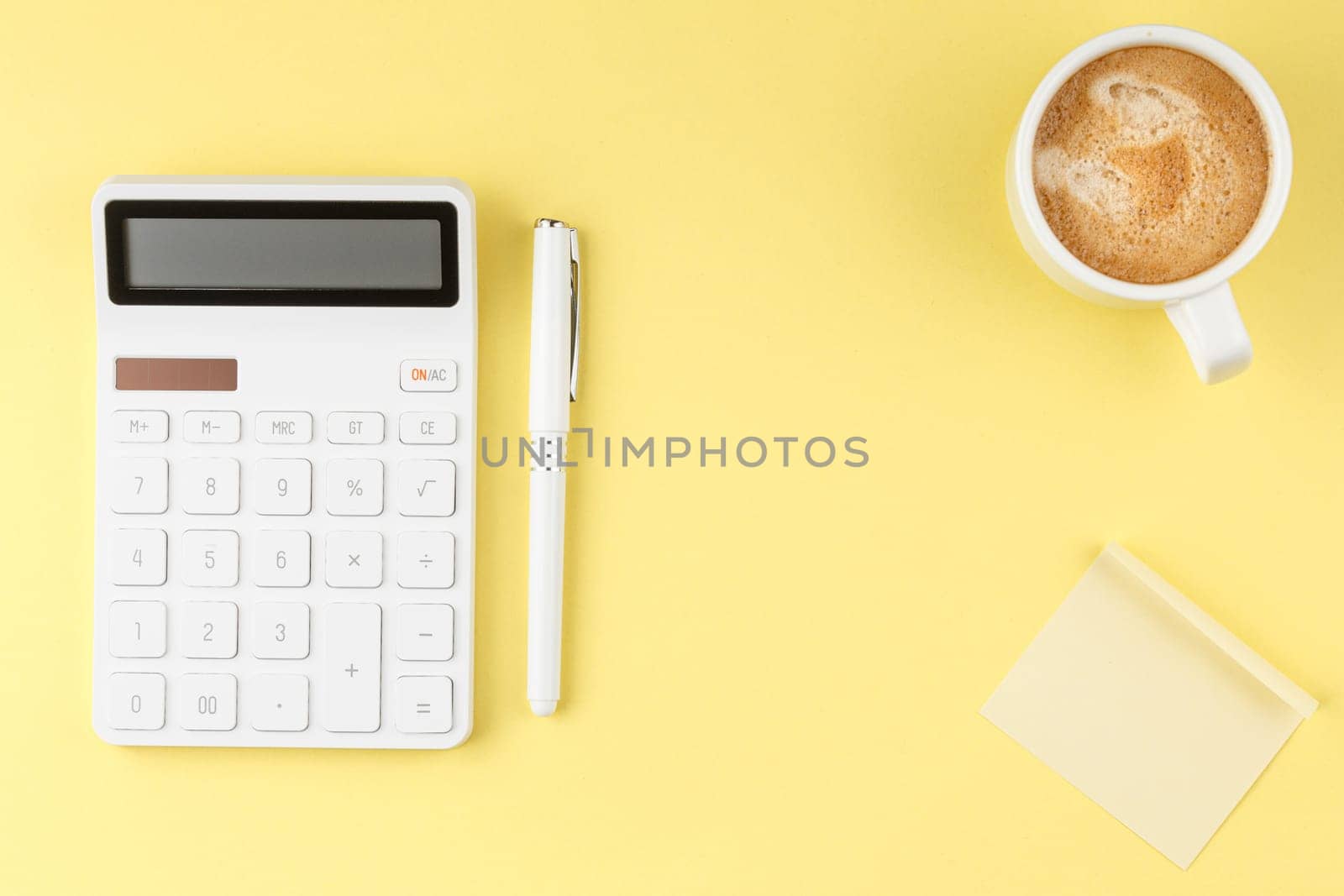 White calculator, coffee cup, pen and note paper on yellow isolated background. Office Concept flat lay