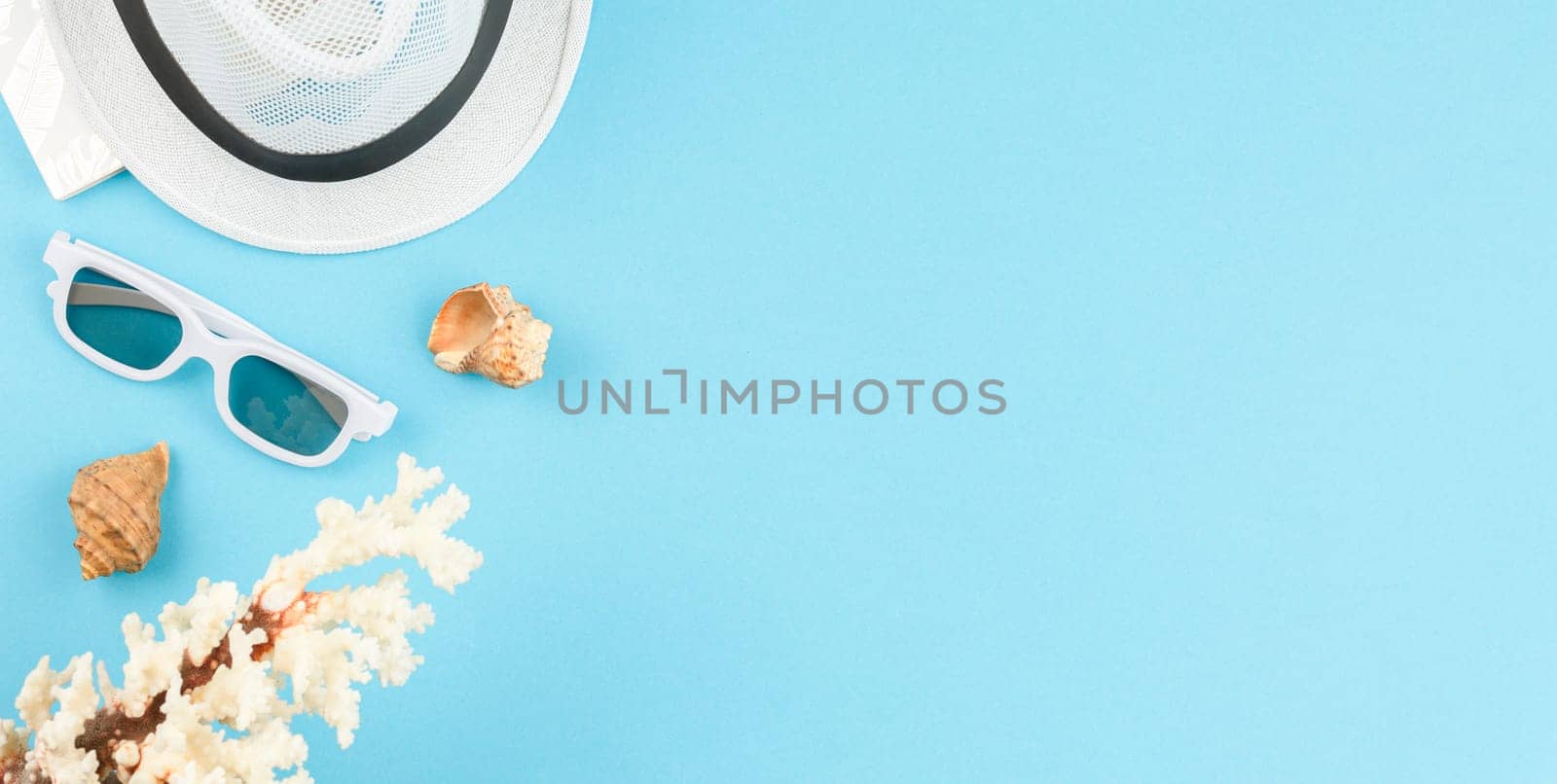 Beach hat with sunglasses on blue isolated background with copy space. Flat lay. Summer vacation concept. Seashells top view.