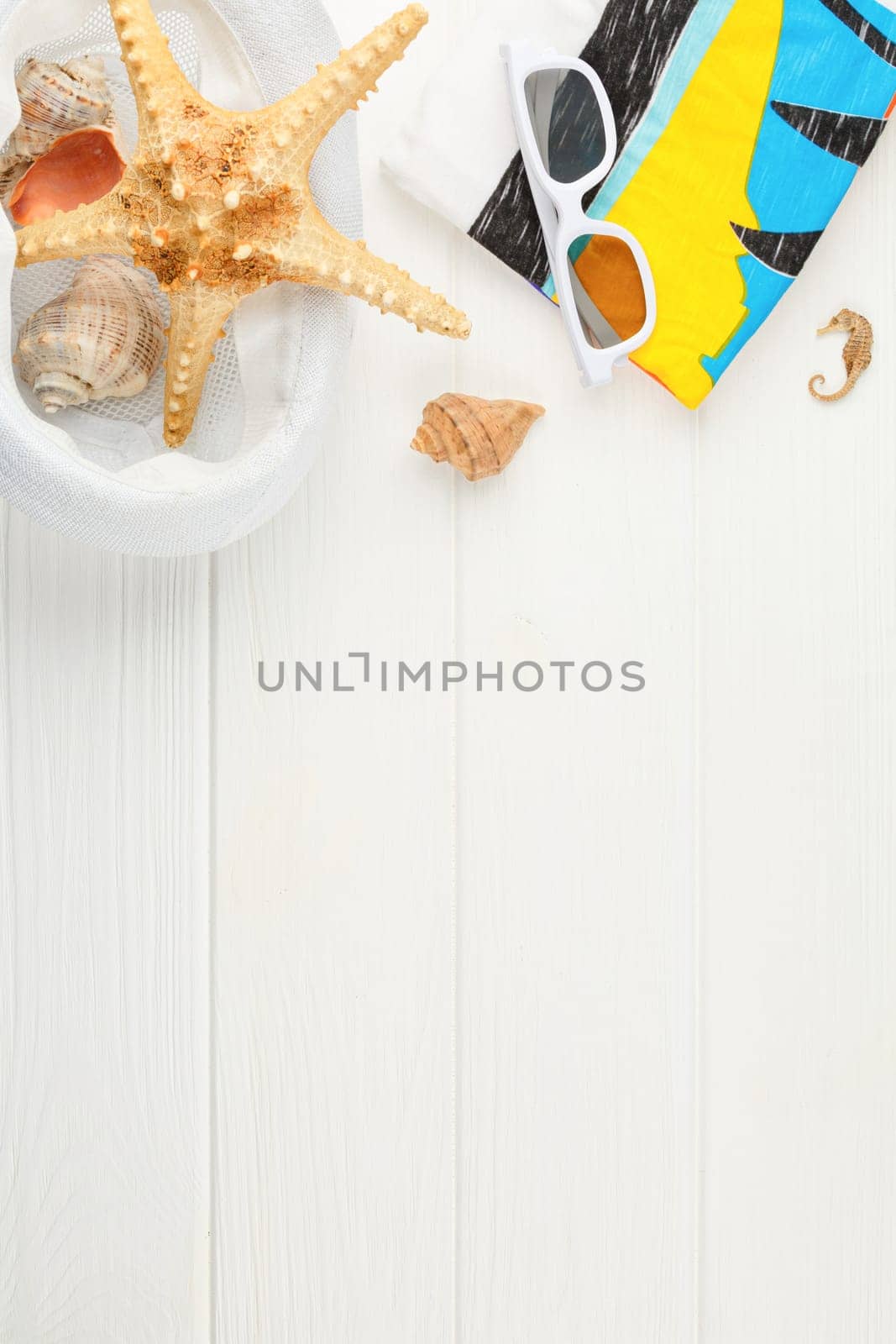 Beach hat with towel and sunglasses on white wooden background. Banner with copy space. Summer vacation concept. Flat lay. Starfish and seashells. Vertical photo.
