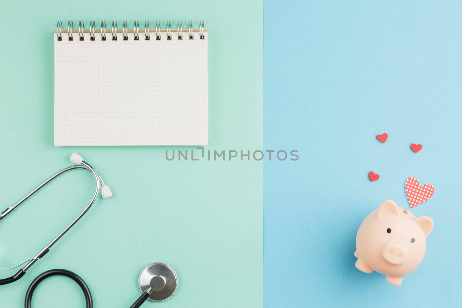 Open spiral notebook. Charity for medicine. Pig piggy bank with red hearts and a stethoscope on a two color background. Donations and volunteering concept. Top view, flat lay.