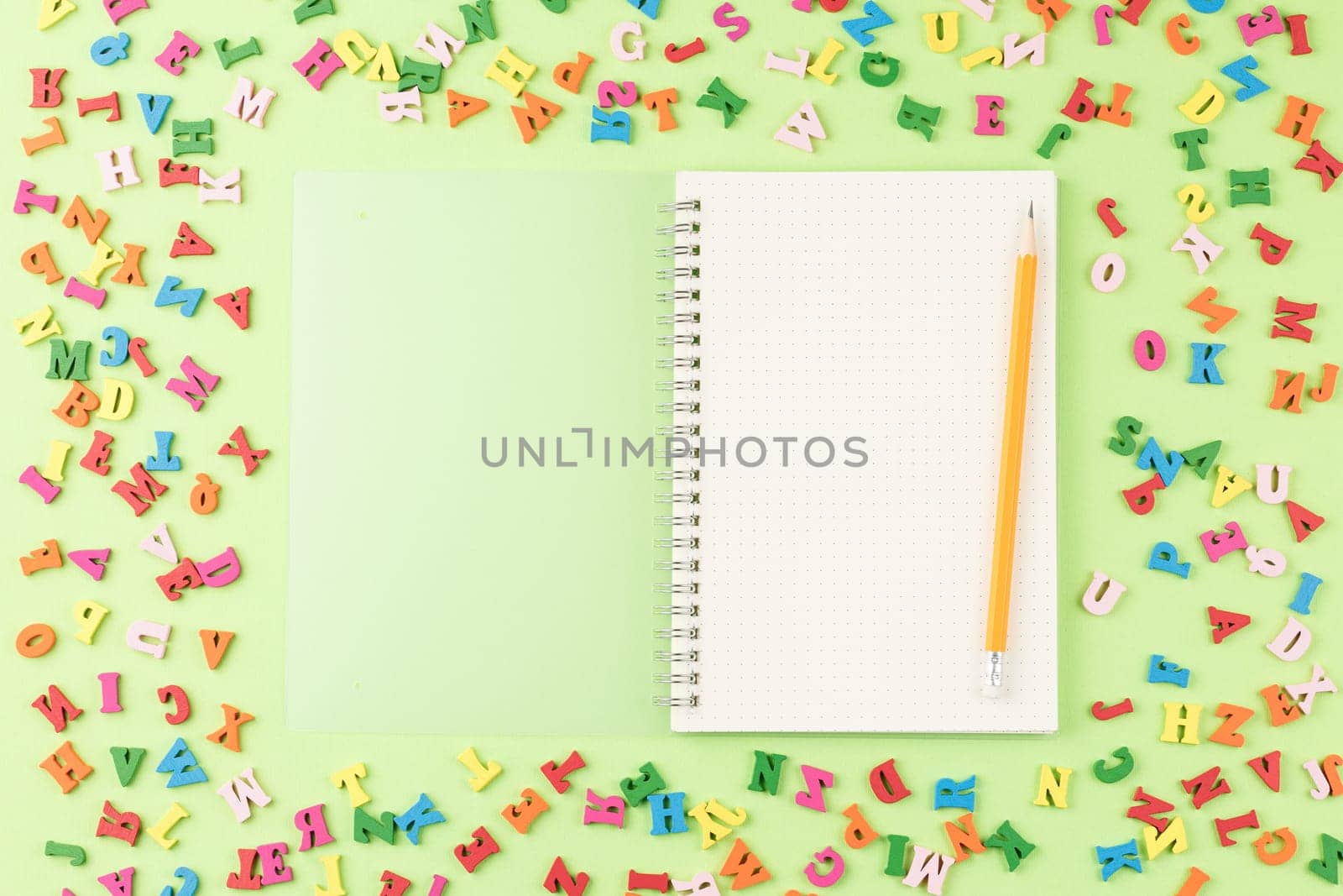 Colored letters of the alphabet on a green background. Top view. Open school notebook with a pencil. Back to school concept.