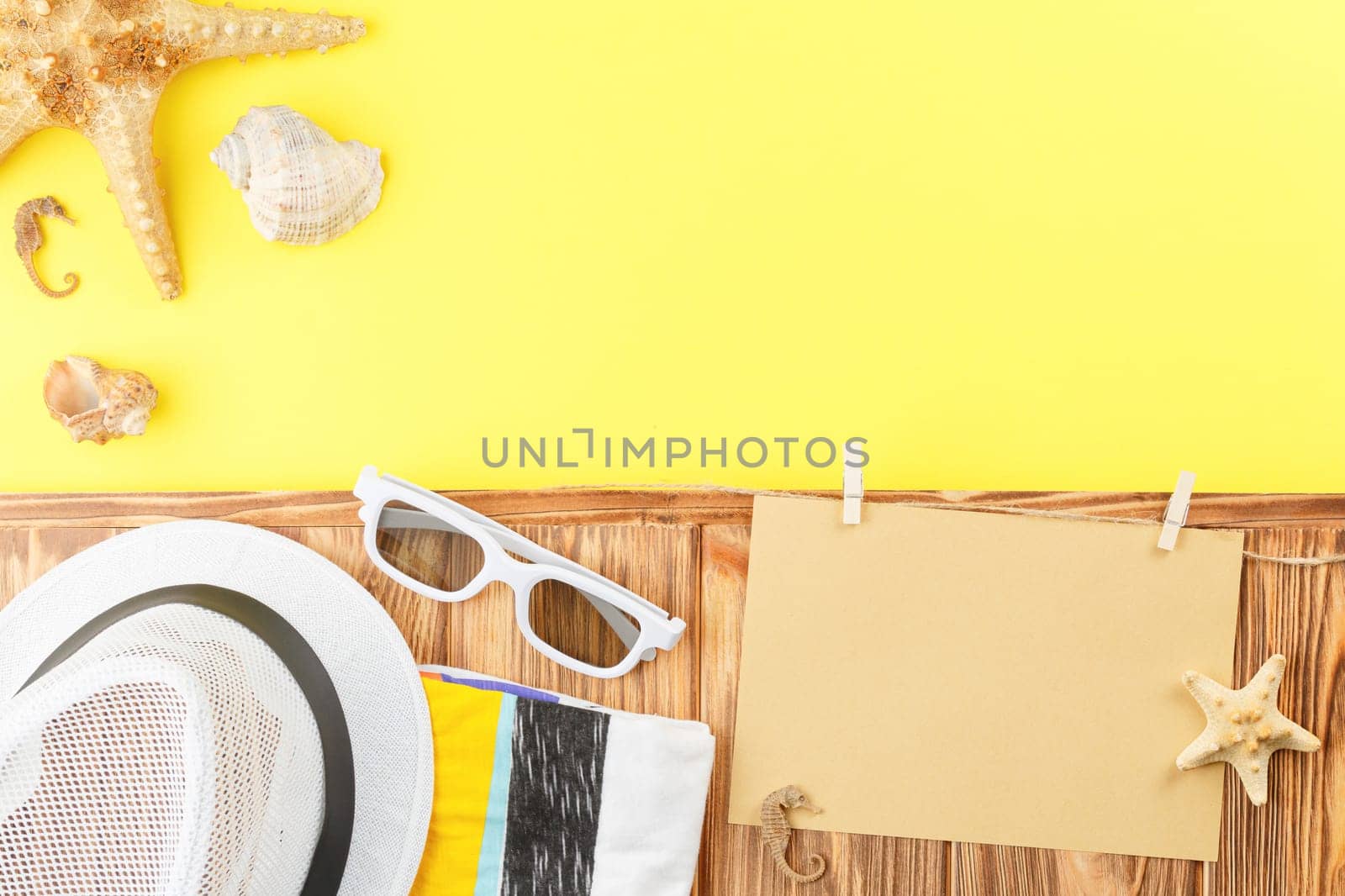 Summer hat with sunglasses and towel on wooden background with yellow copy space. Flat lay. Beach vacation concept. Starfish and seashell. Top view.