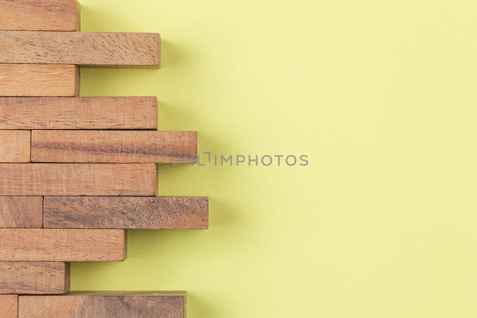 Wooden blocks lined in the form of a brick wall on yellow background. Top view.