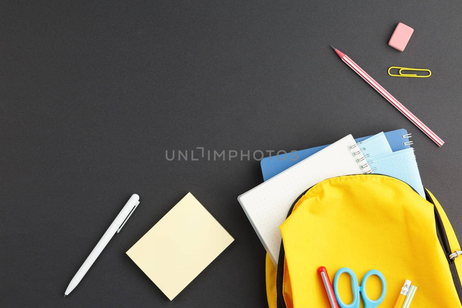 School backpack with notebooks and supplies on a blackboard background. Top view. Back to school concept. Flat lay.
