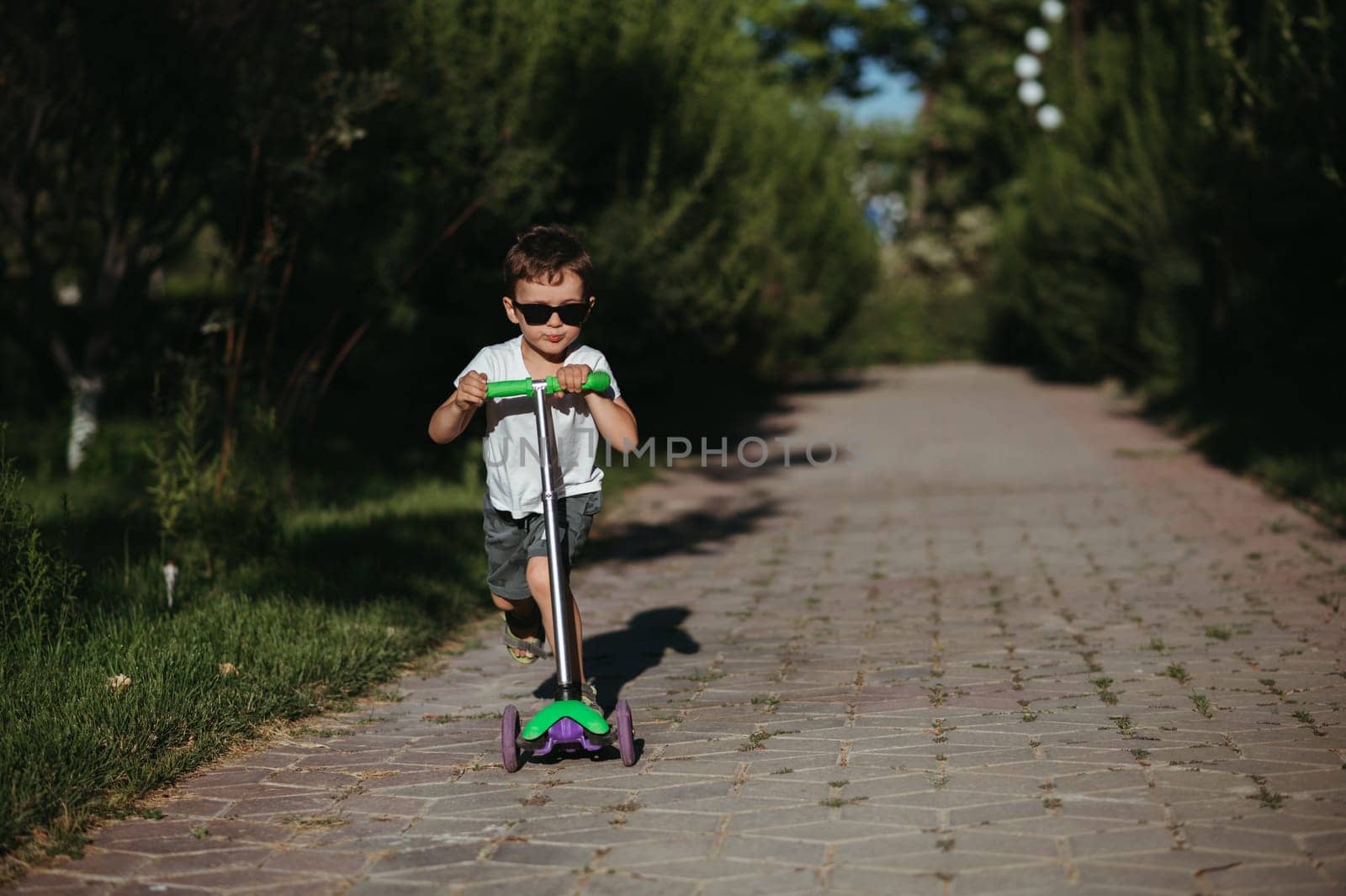 preschooler boy rides a scooter in the park in the summer
