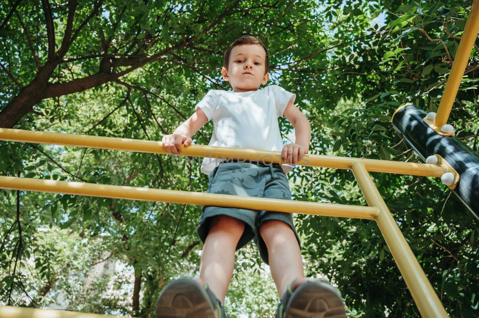 child boy playing and climbing on horizontal bars on the playground in summer
