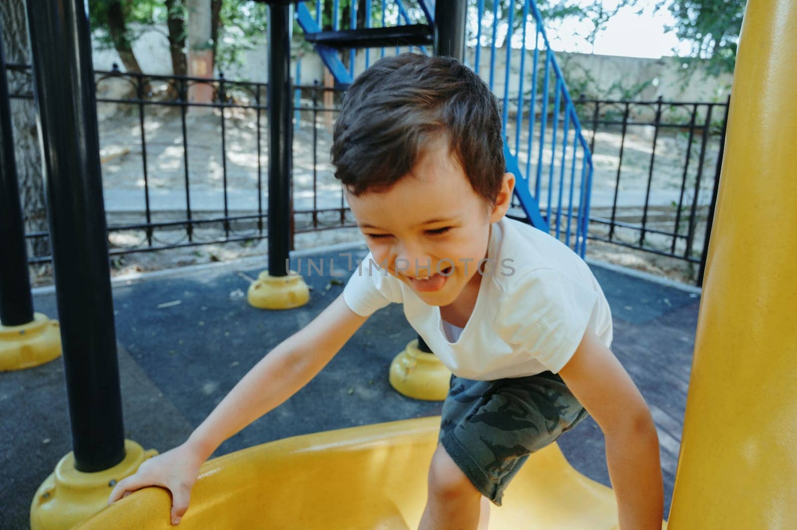 happy child kindergarten boy playing on a slide on the playground in summer